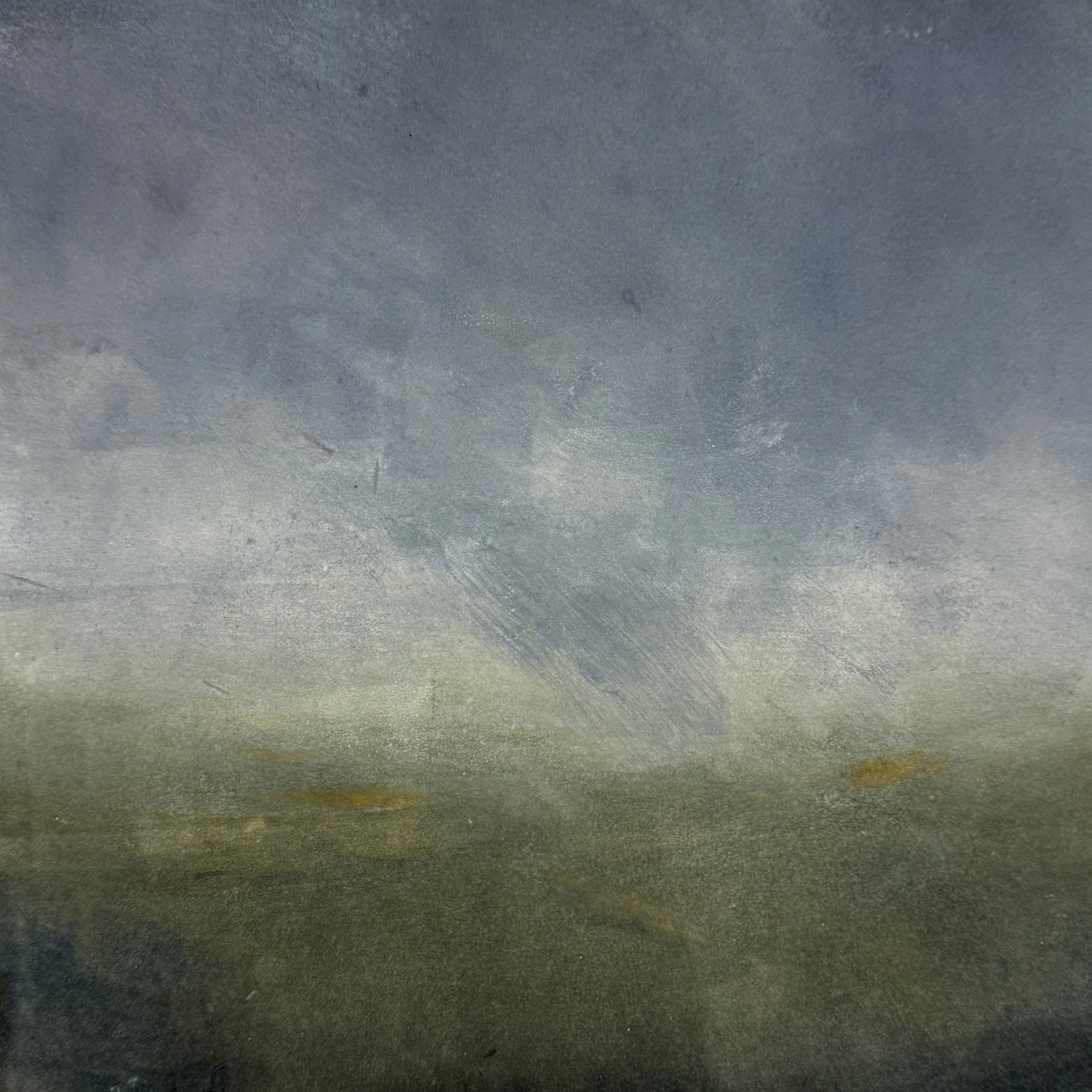 Close-up photo of a textured surface with a gradient of colors from dark gray to lighter shades of gray, yellow, and green at the bottom.