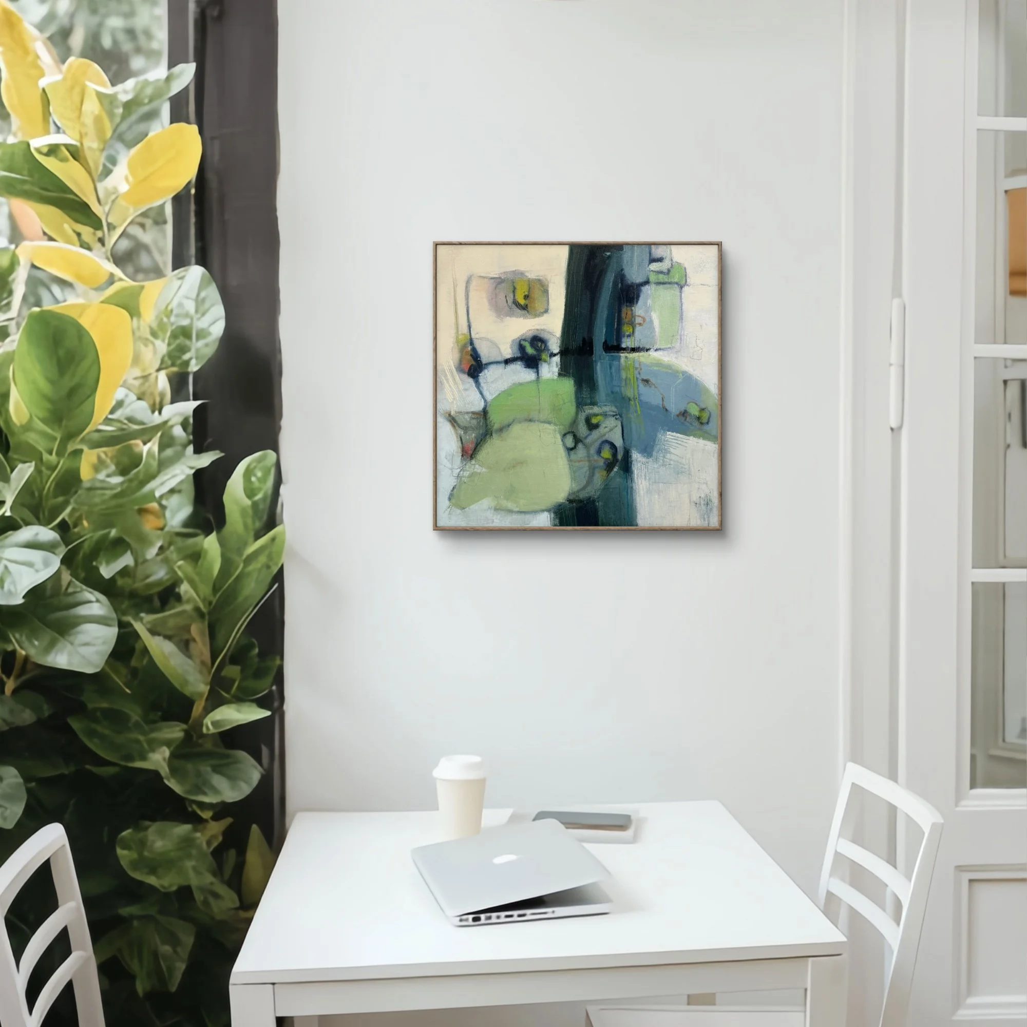 Interior of a modern room with a white table and chairs, a large leafy plant on the left, a colorful abstract painting on the wall, a coffee cup on the table, and a laptop.