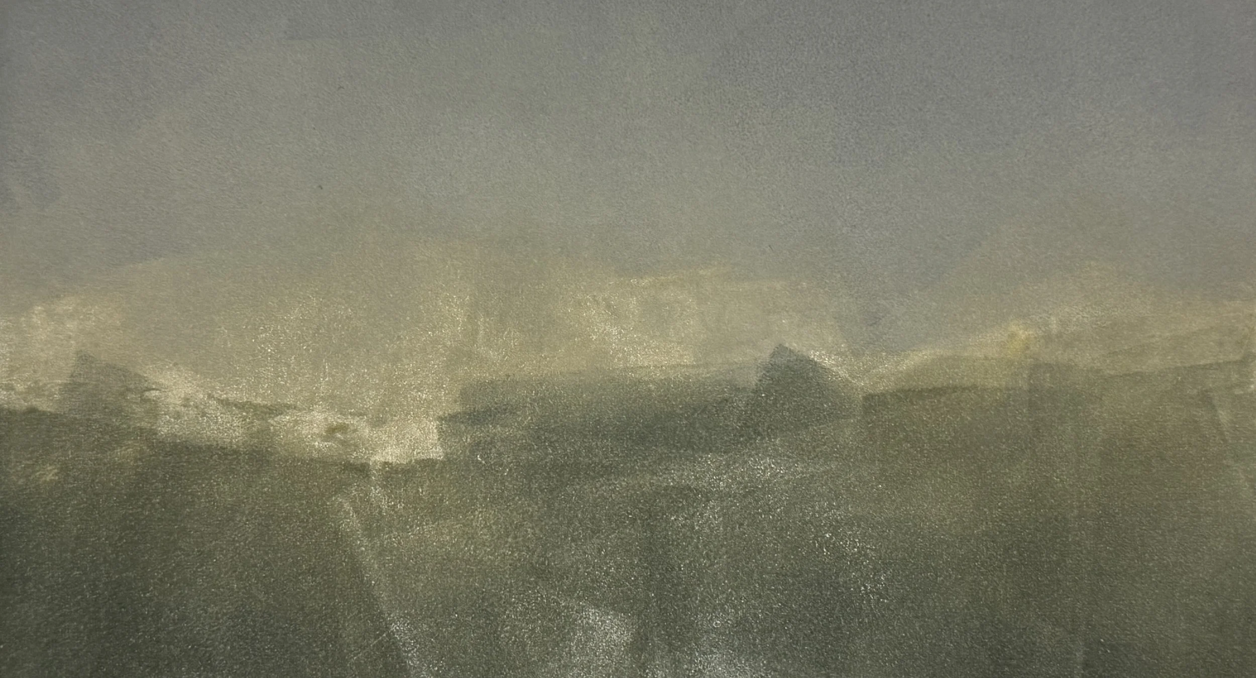 A foggy or misty landscape with darkened mountains or hills in the distance and overcast sky.