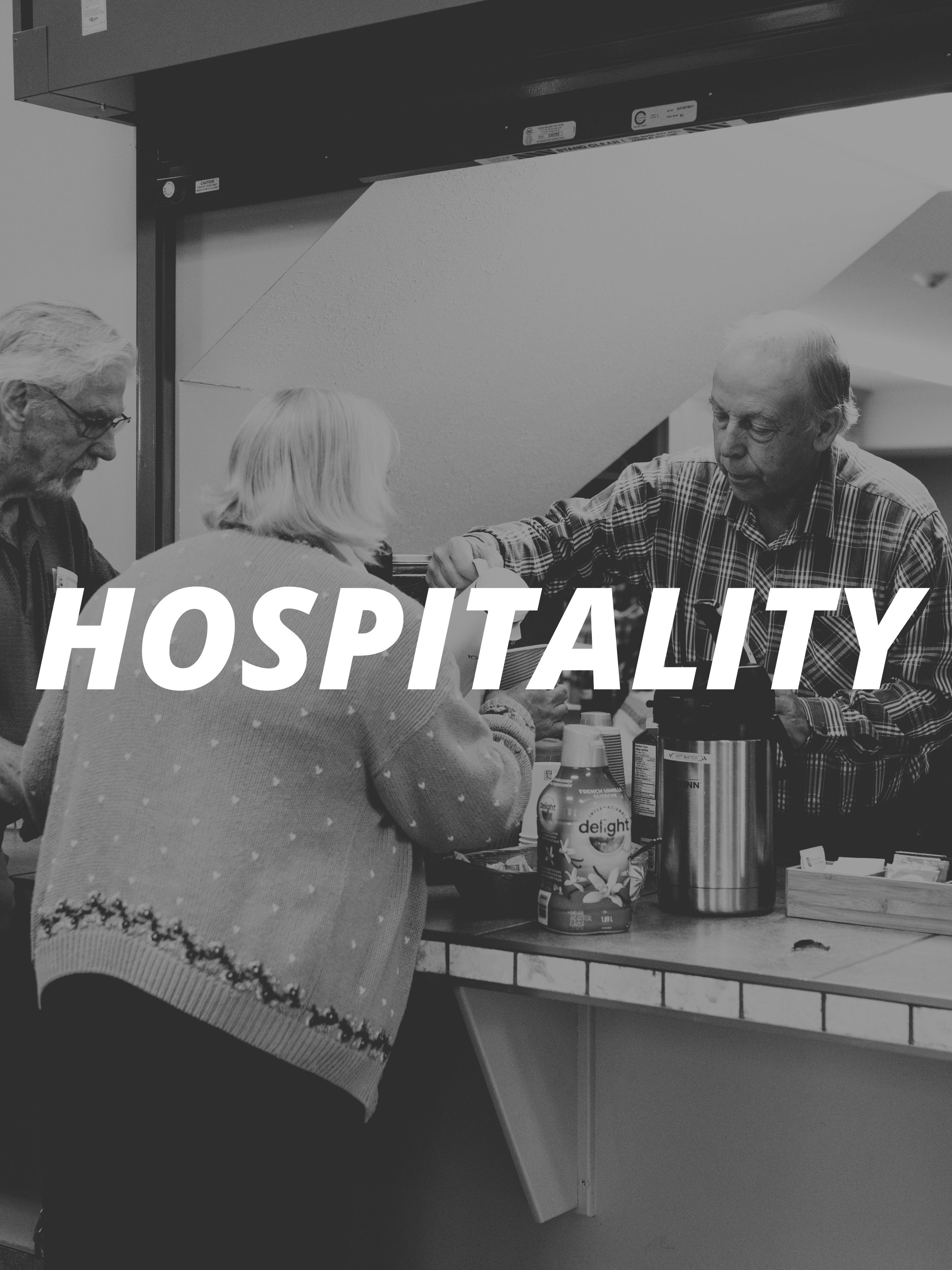 Three elderly people gathered around a table with a beverage container, a juice carton, and a tray of snacks, in a hospital hospitality area.