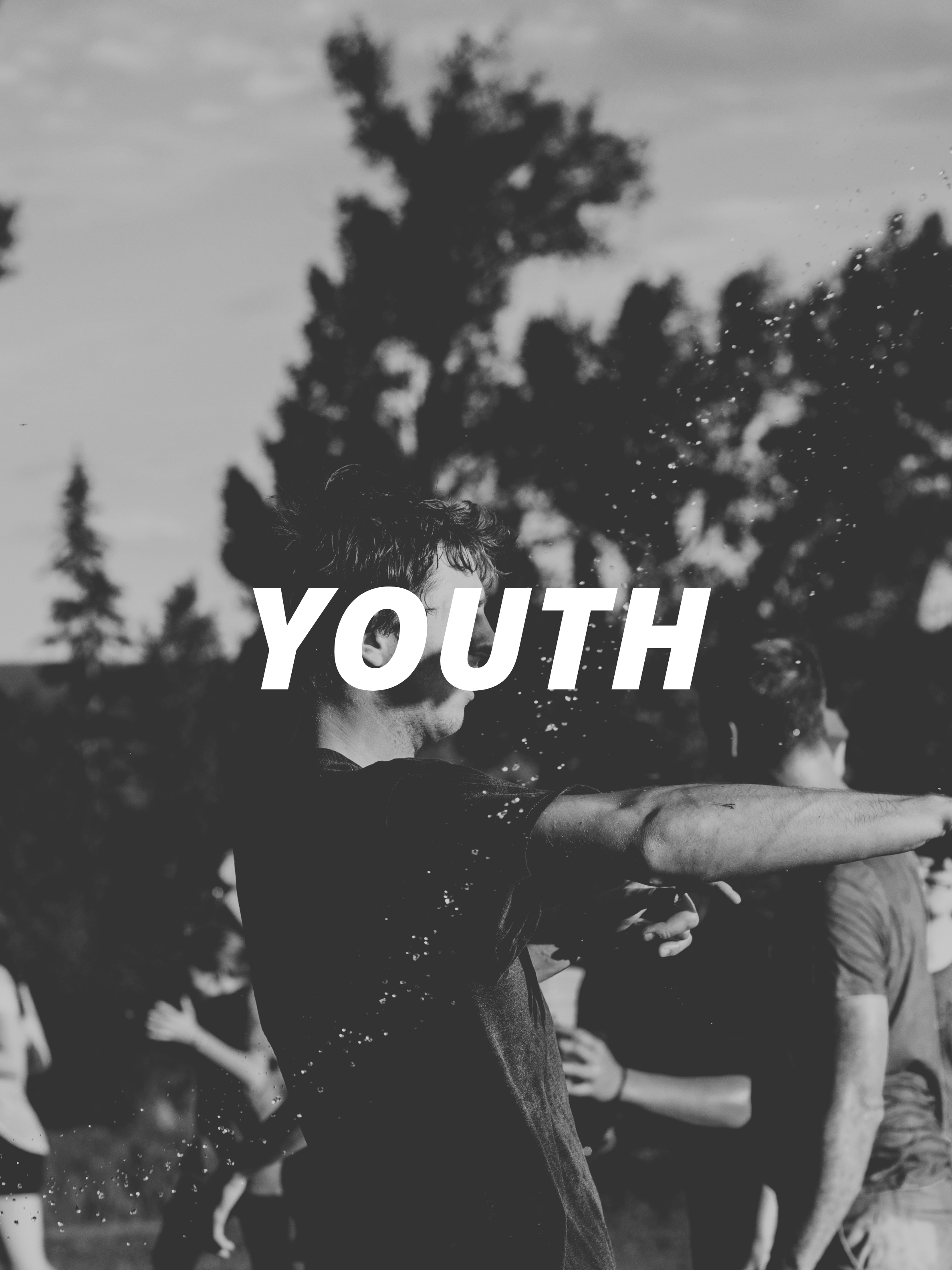A group of young people participating in an outdoor activity, stretching or exercising, with trees in the background, in black and white.