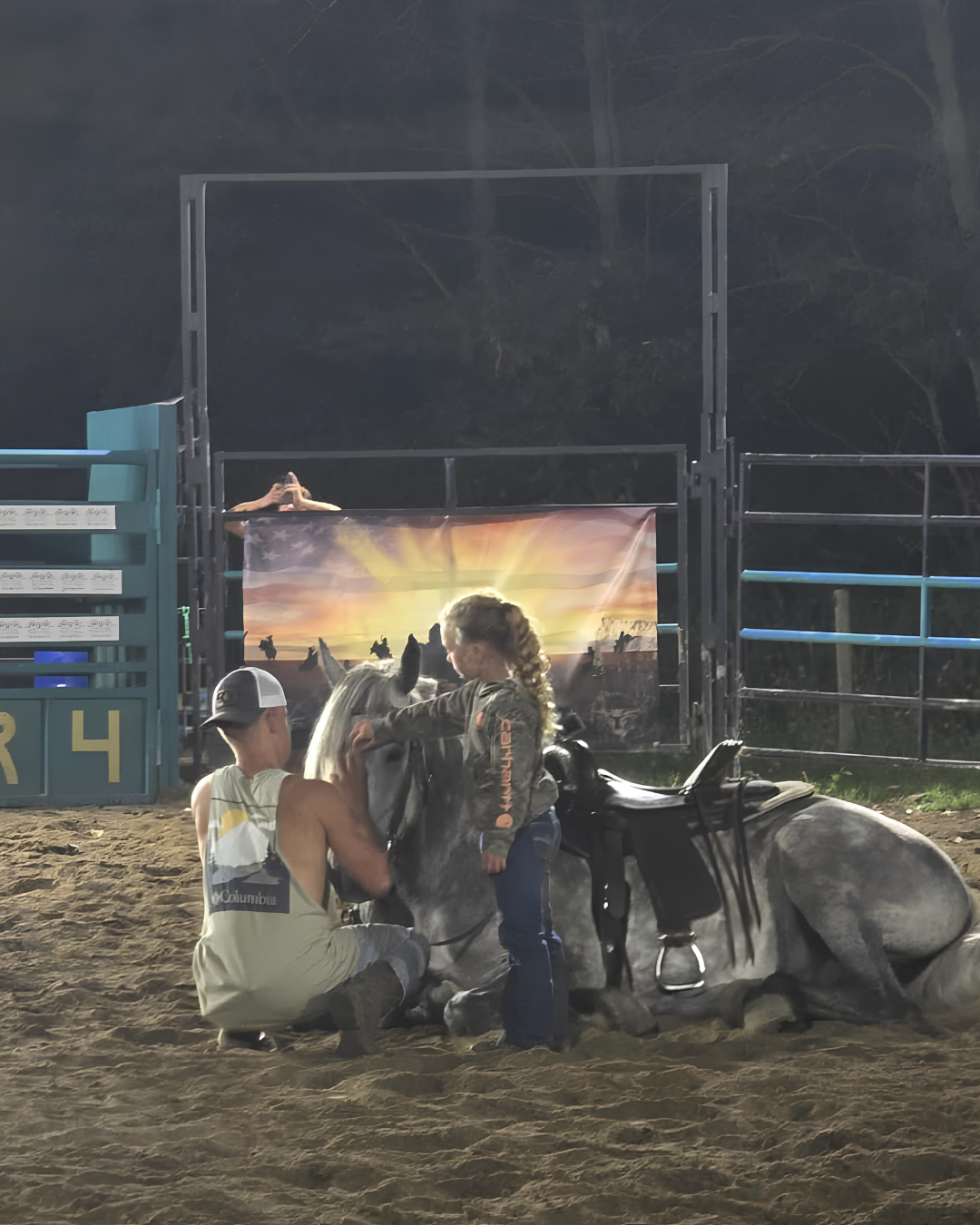A young girl and a boy with a horse at an outdoor rodeo arena at sunset.