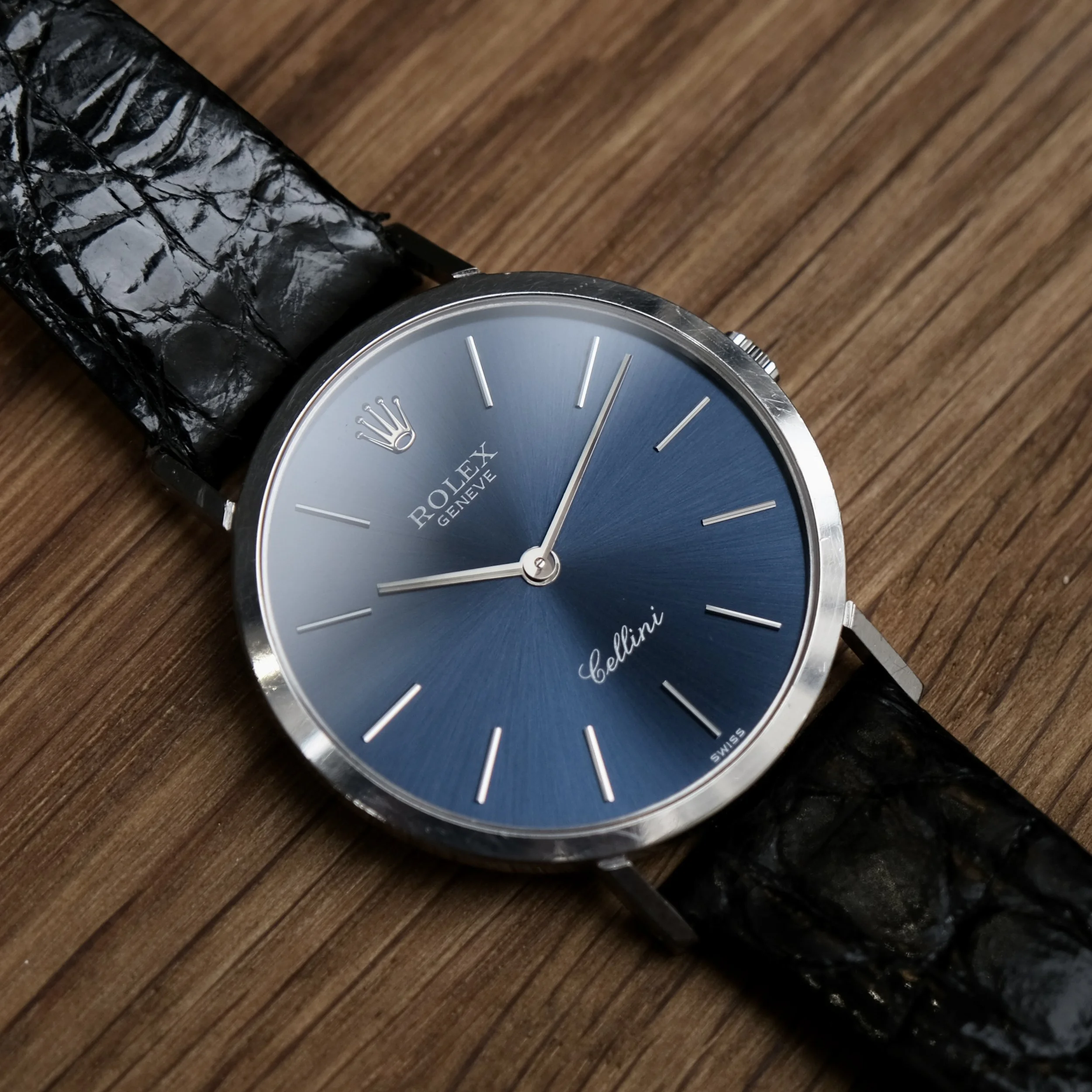 Montre Rolex avec un bras en crocodile noir et un cadran bleu, posé sur une surface en bois.