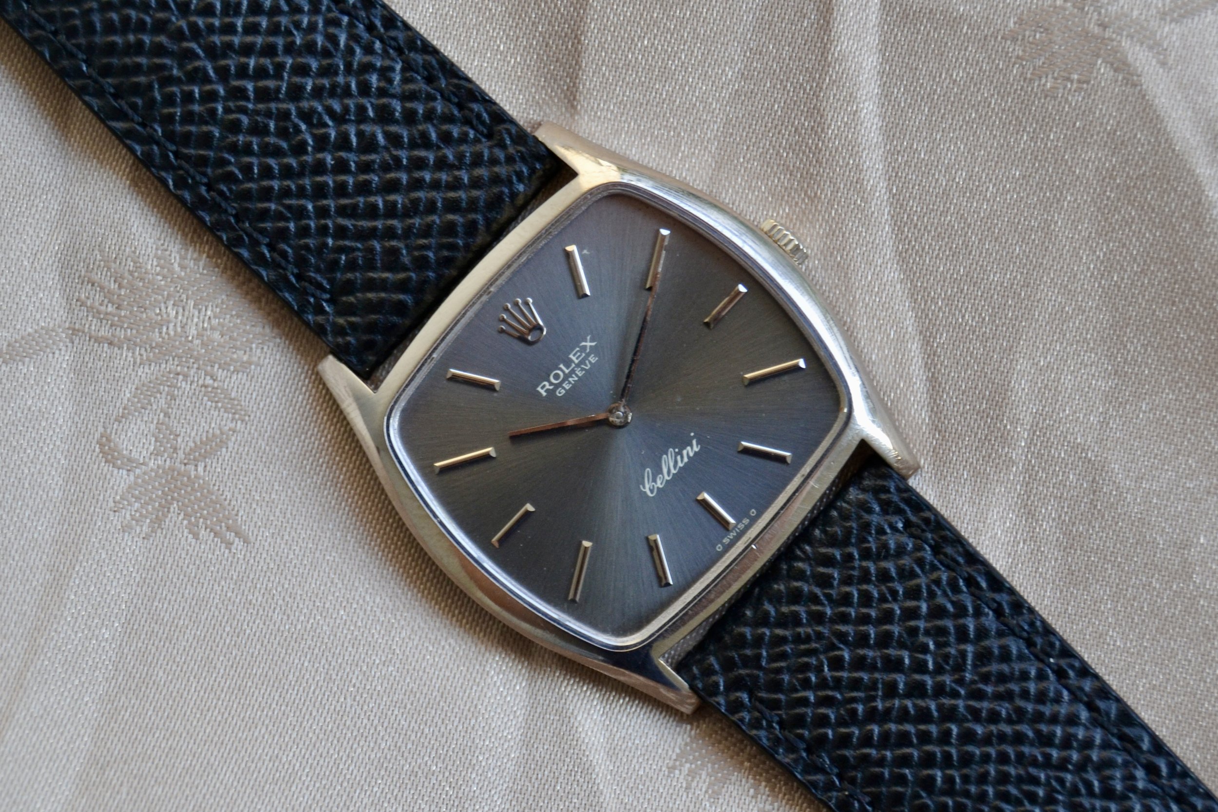 Montre Rolex Geneva avec un bracelet en cuir noir texturé posée sur un tissu beige avec un motif floral discret.