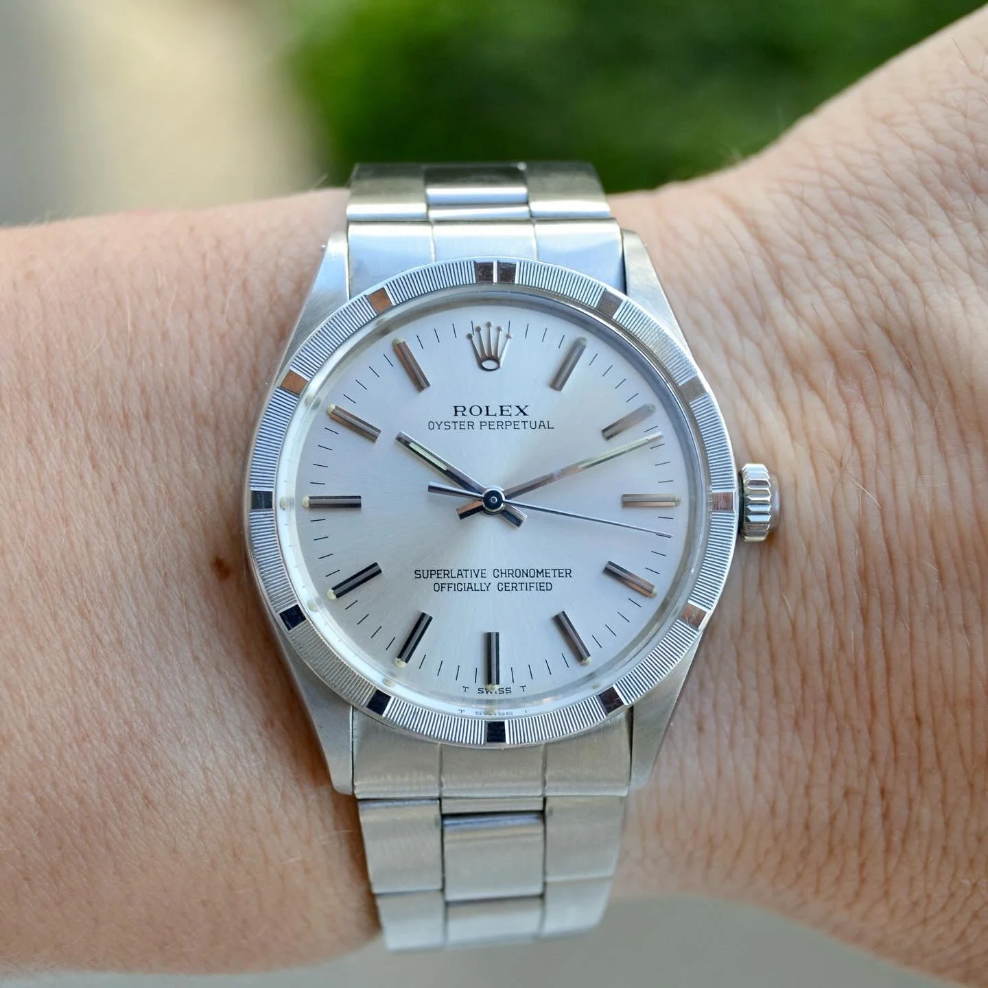 Montre Rolex Oyster Perpetual avec bracelet en métal, cadran argenté, index en bâtons, et trois aiguilles, portée au poignet d'une personne.