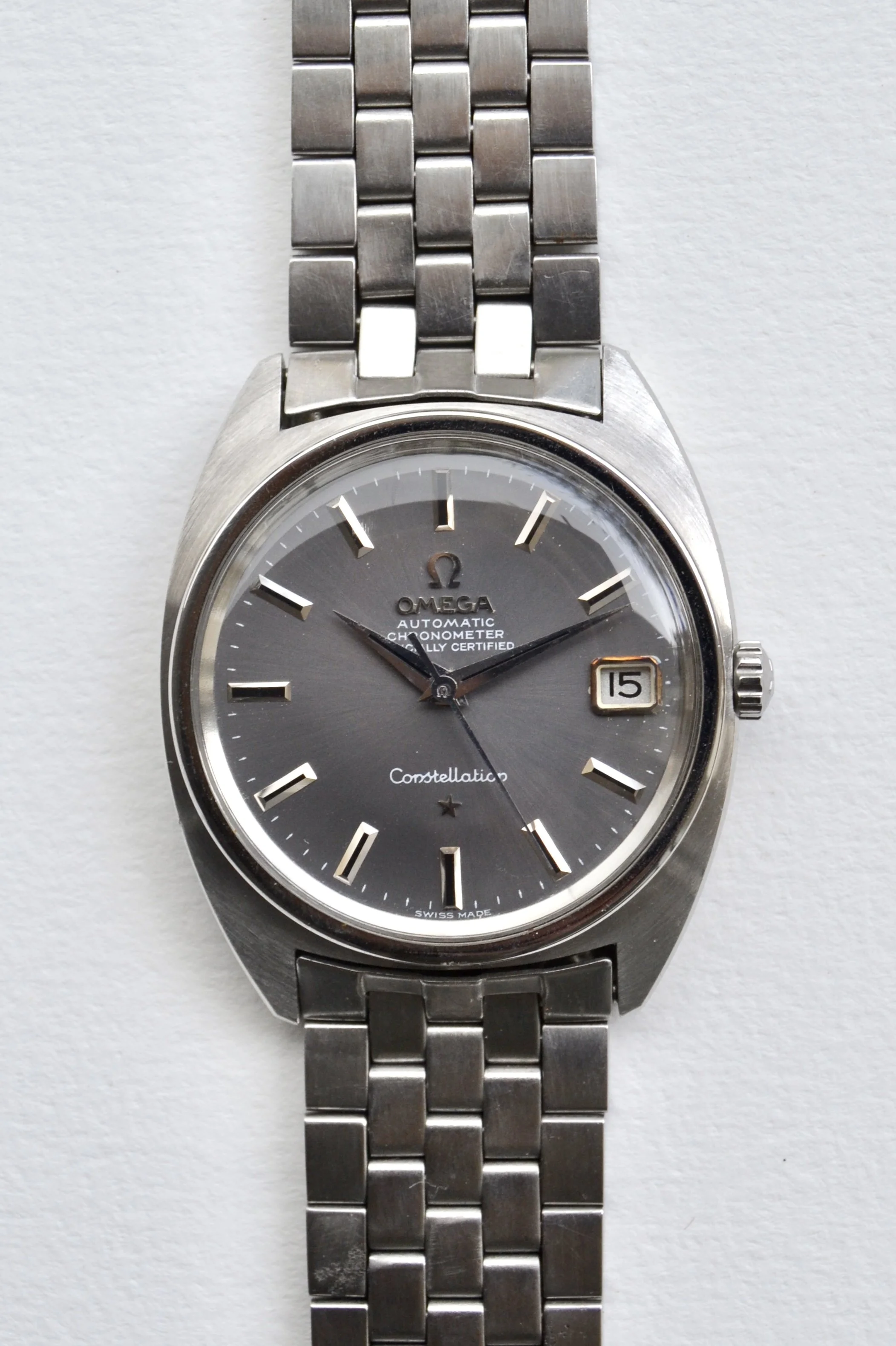 Montre Omega Astroconstellation en acier inoxydable avec aiguilles noires, cadran gris, date à 3 heures, et bracelet en maillons.