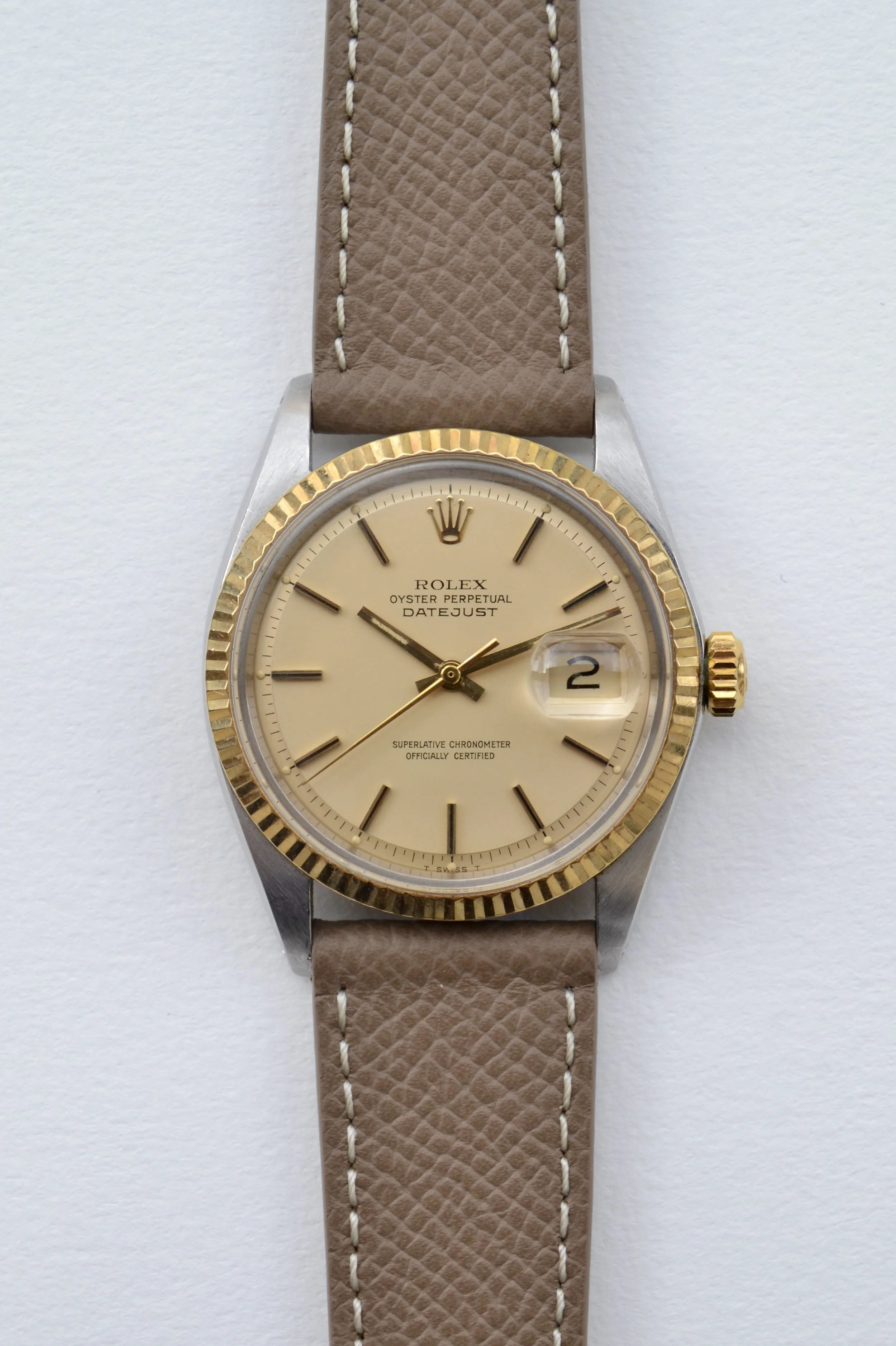 Montre Rolex avec cadran beige, lunette or, bracelet en cuir beige avec couture blanche, affichant la date.