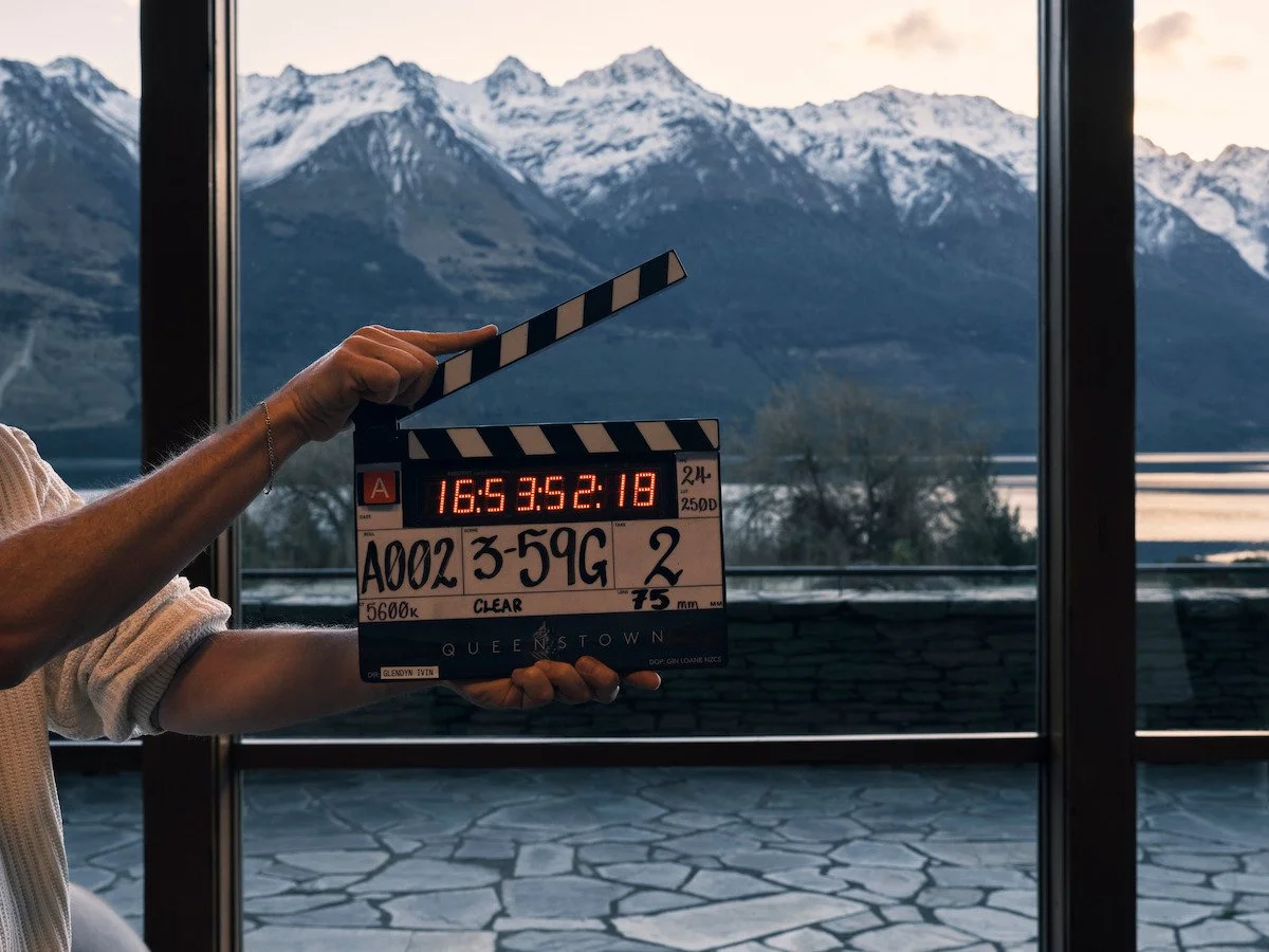 A person holding a film clapboard with a mountain landscape in the background