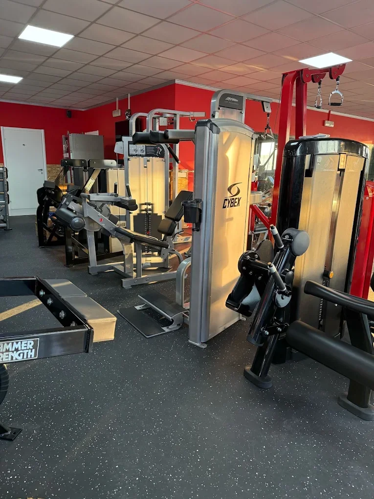 Macchinari da palestra in una palestra, inclusi attrezzi per allenamenti di resistenza e esercizi di forza, con pavimentazione nera e pareti rosse.