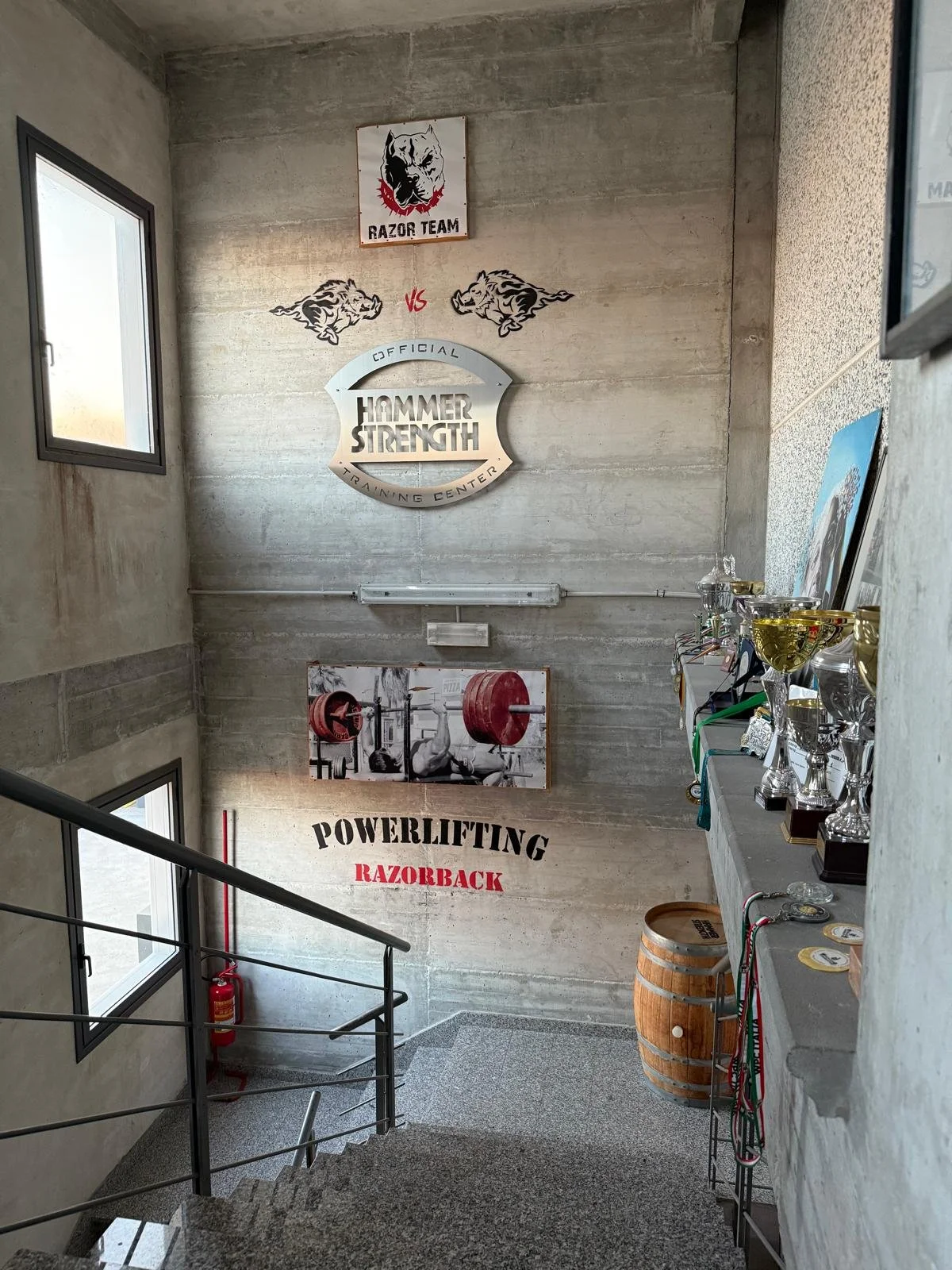 Interno di una palestra con pareti in cemento, con decorazioni sportive, premi e un'immagine di sollevamento pesi, destinate al powerlifting, con un'area riservata alla competizione Razorback.