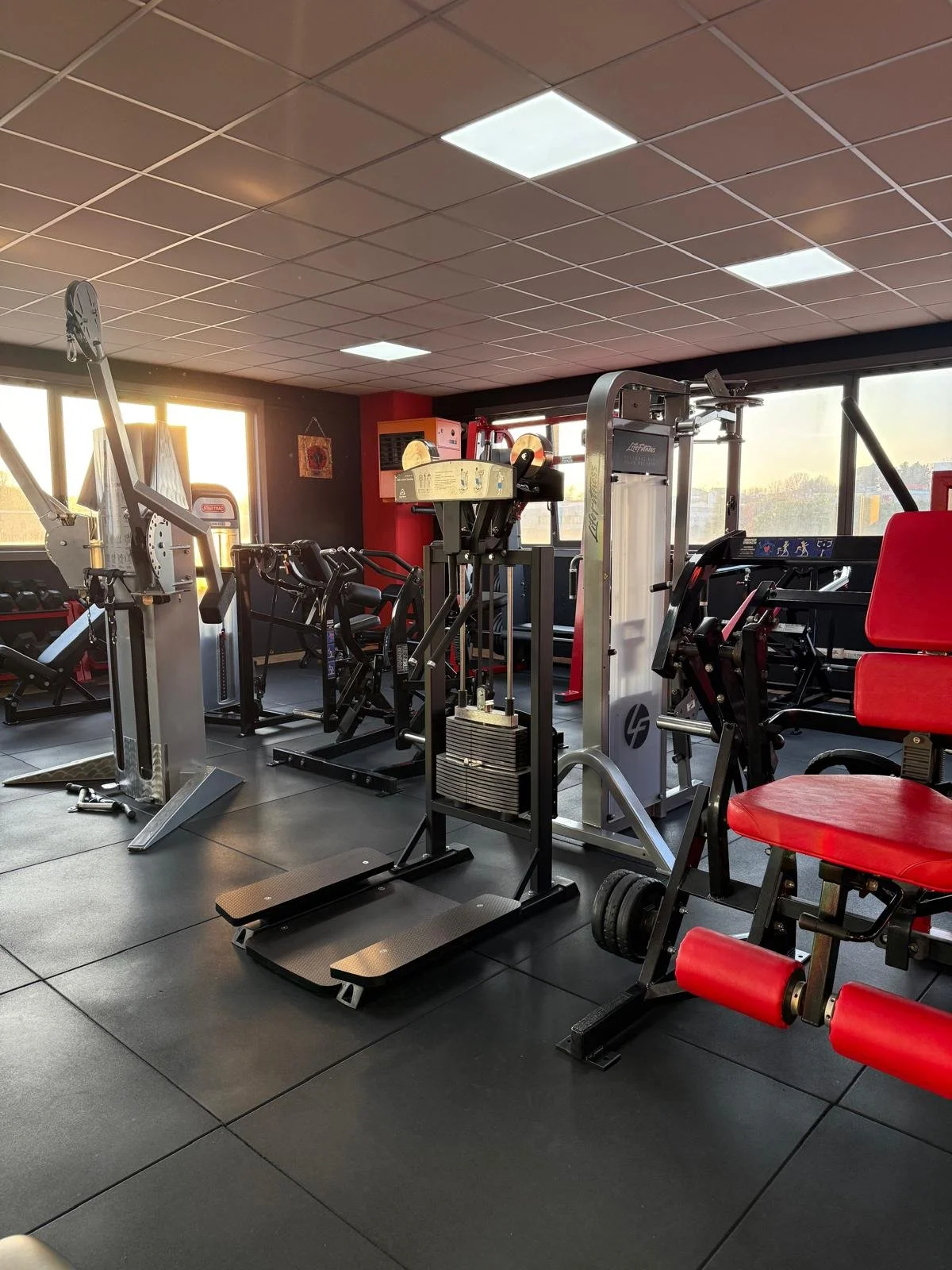 Palestra con attrezzi ginnici, come tapis roulant, cyclette, e macchina per pesi, illuminata dalla luce del tramonto attraverso le finestre.