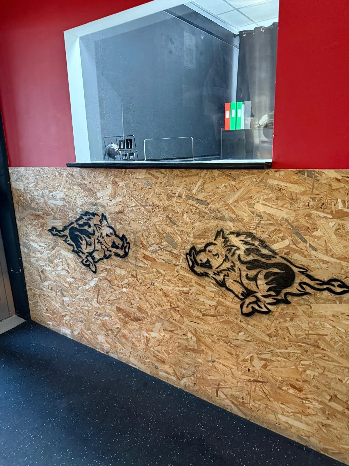Vista di un bancone in legno con grafiche di cani, dietro una finestra in vetro e pannelli di cartone. Il pannello di legno ha disegni di cani disegnati con linea nera.