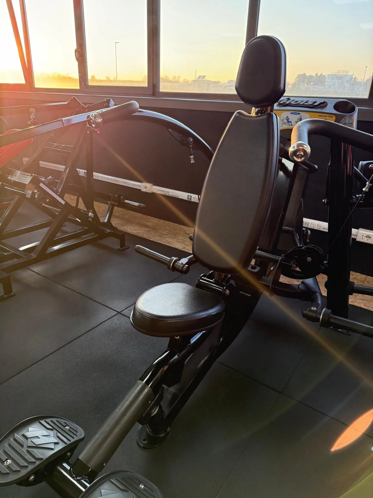 Attrezzi da palestra vicino a una finestra con vista al tramonto, incluse una cyclette e un tapis roulant.
