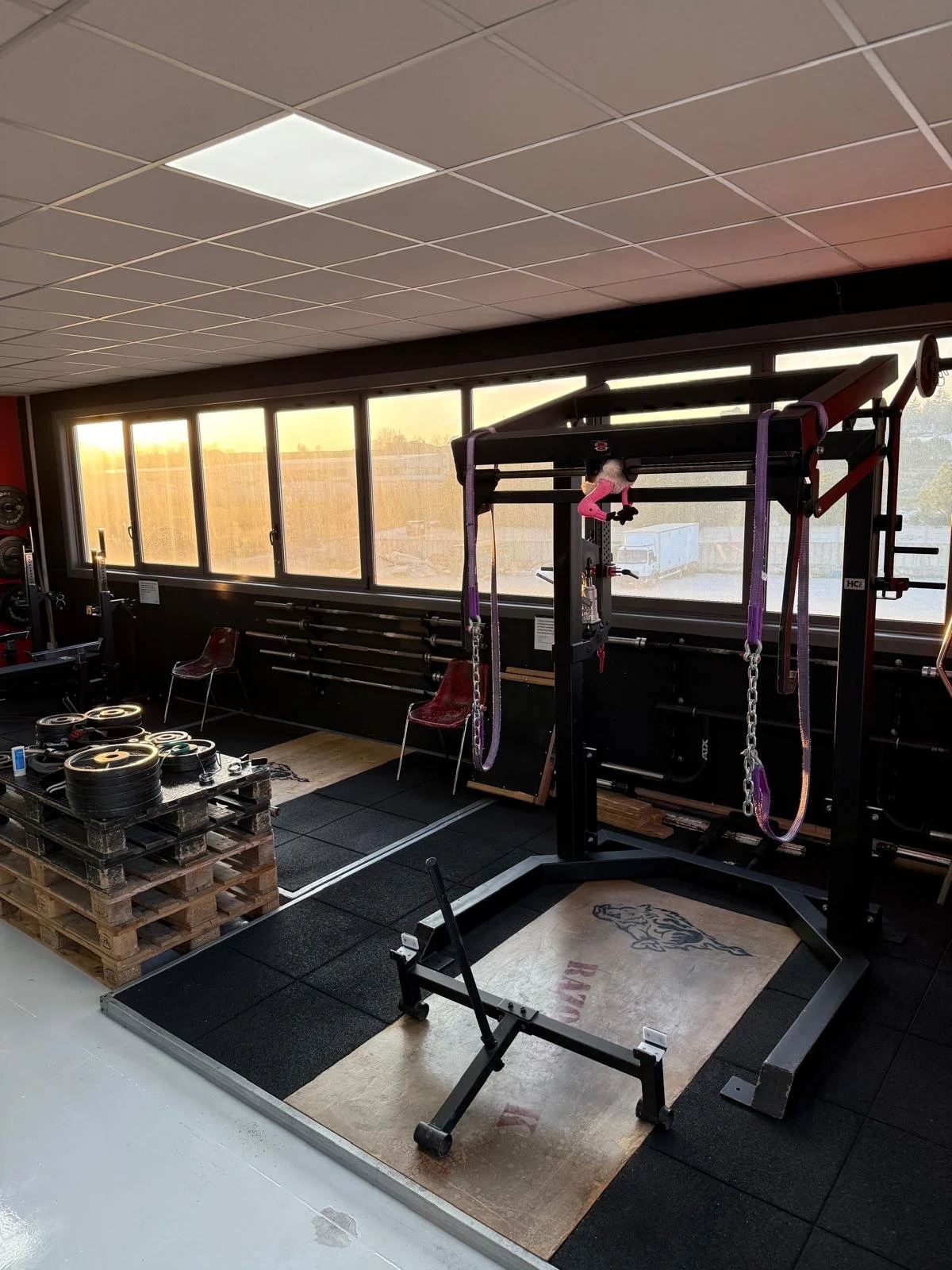 Una palestra con attrezzature per il sollevamento pesi, come dischi e barre, e un'area di sollevamento con una macchina per trazioni e una pedana per sollevamento.