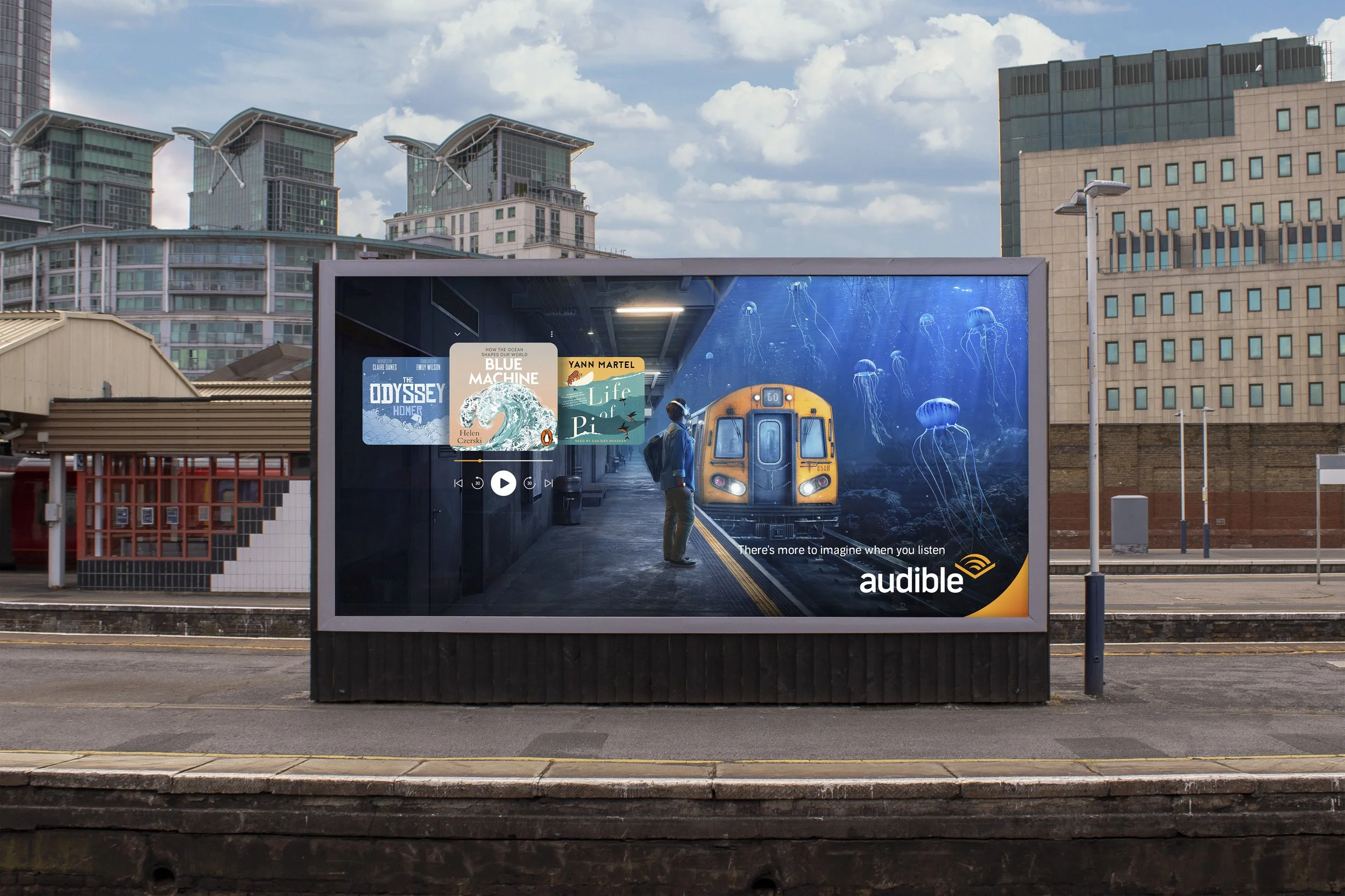 A train station platform with an advertisement for Audible, featuring a scene of a person standing before a mural of jellyfish in an underwater train station, with city buildings and a partly cloudy sky in the background.