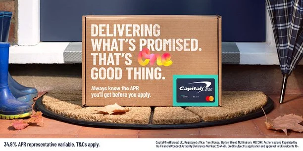 Delivery box with Capital One logo on doorstep, surrounded by fallen leaves and rubber boots.