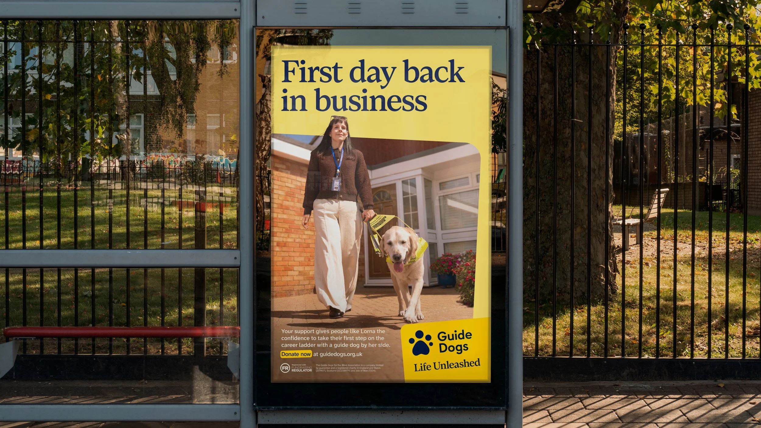 A poster on a bus stop featuring a woman walking a guide dog outside a building. The poster promotes Guide Dogs with the slogan 'Life Unleashed' and encourages donations.