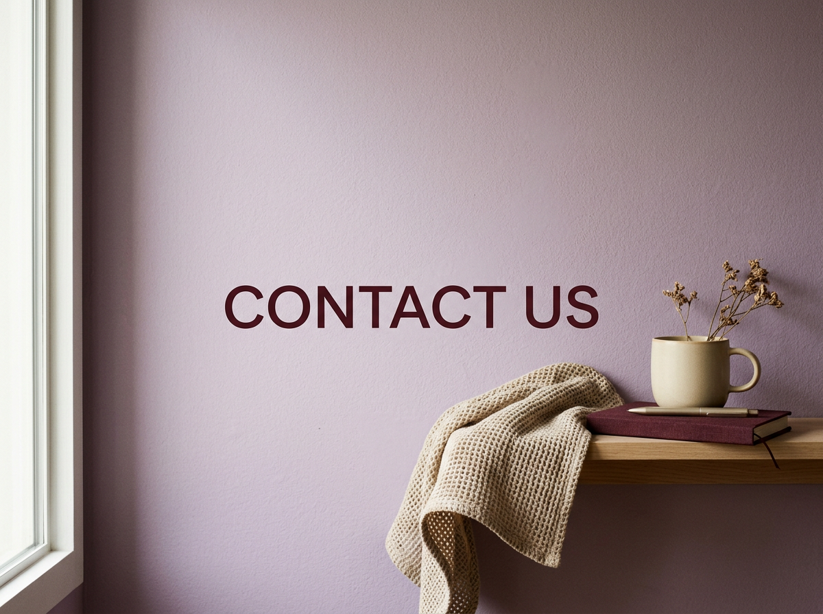 A wall with the words 'CONTACT US' written on it, near a wooden shelf holding a mug with dried flowers, a closed book, and a blanket.