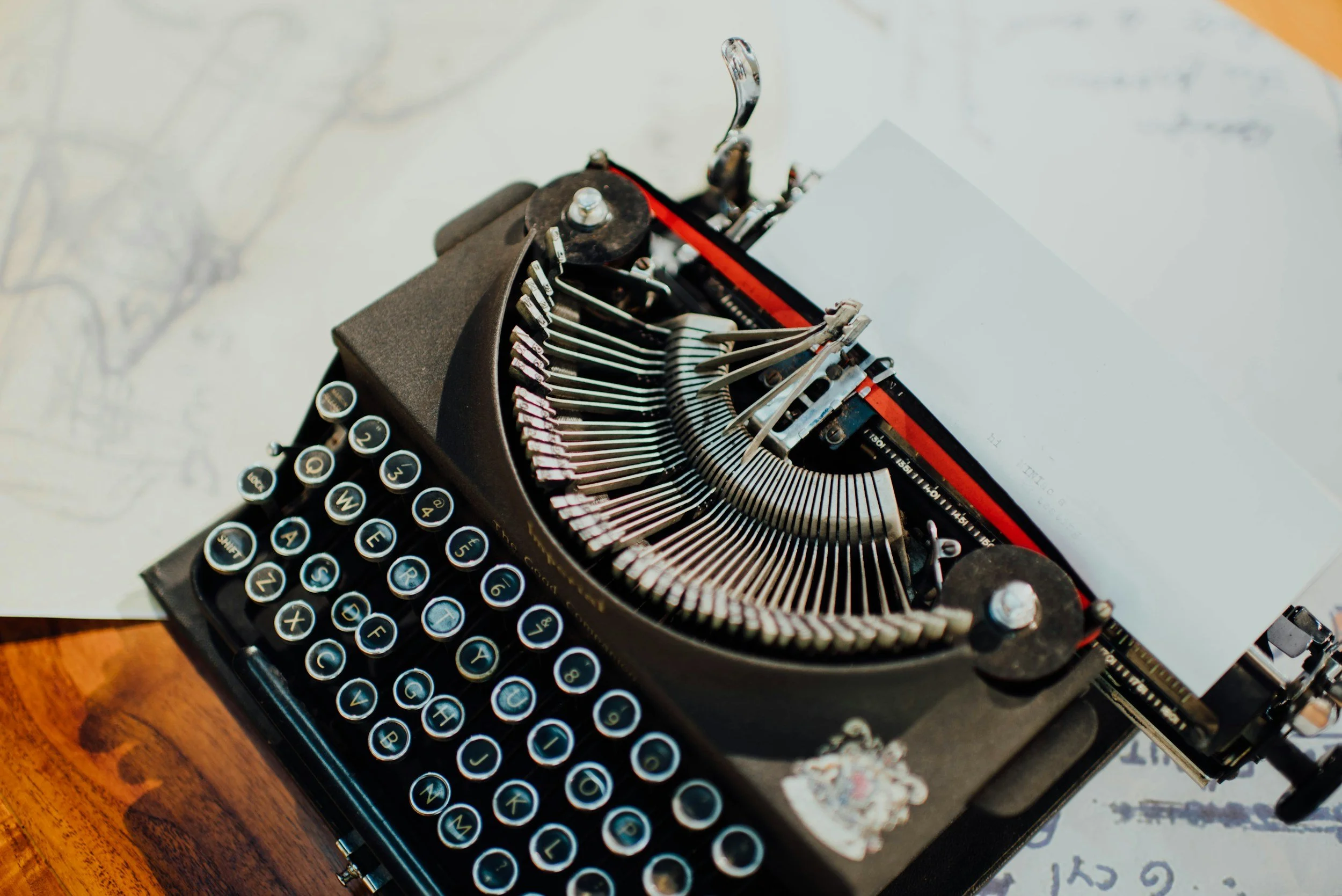 Close-up of a vintage typewriter with black keys and white letters, placed on a wooden surface with paper underneath.