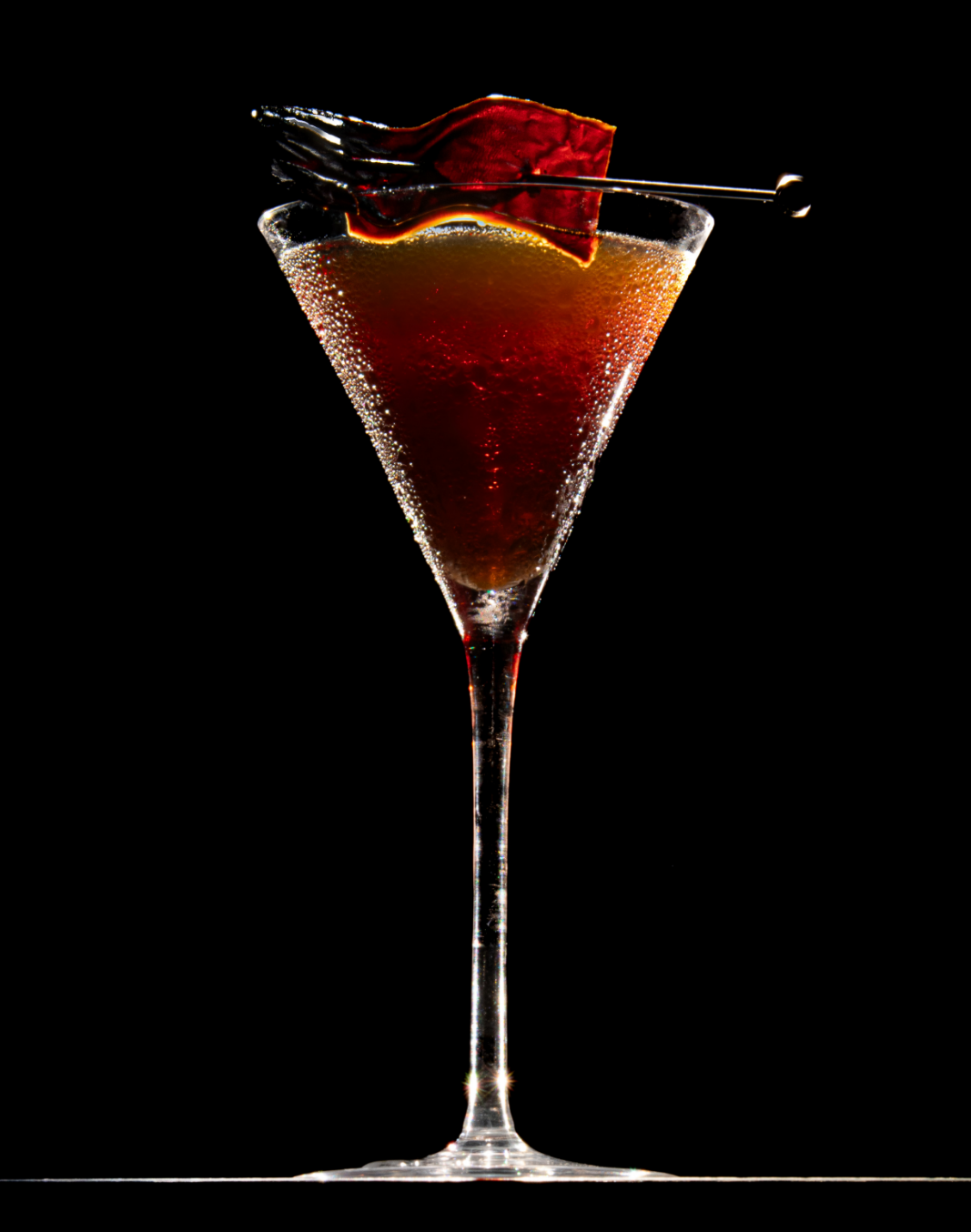 A cocktail in a tall champagne glass garnished with a red cherry and an orange peel, with bubbles rising in the drink, set against a black background.

Leather and bad decisions craft cocktail
