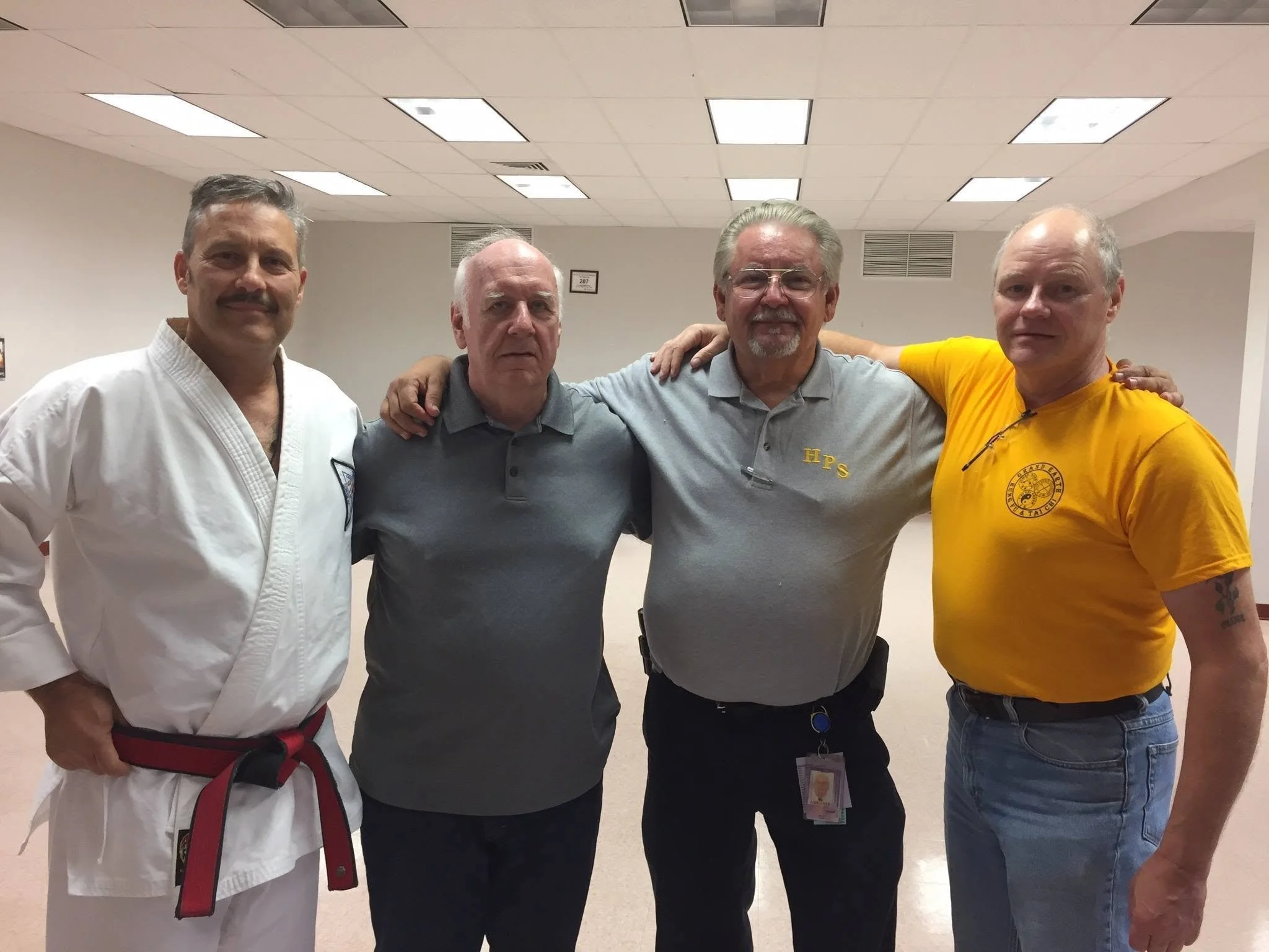 Four men standing together in a room, smiling and with their arms around each other.