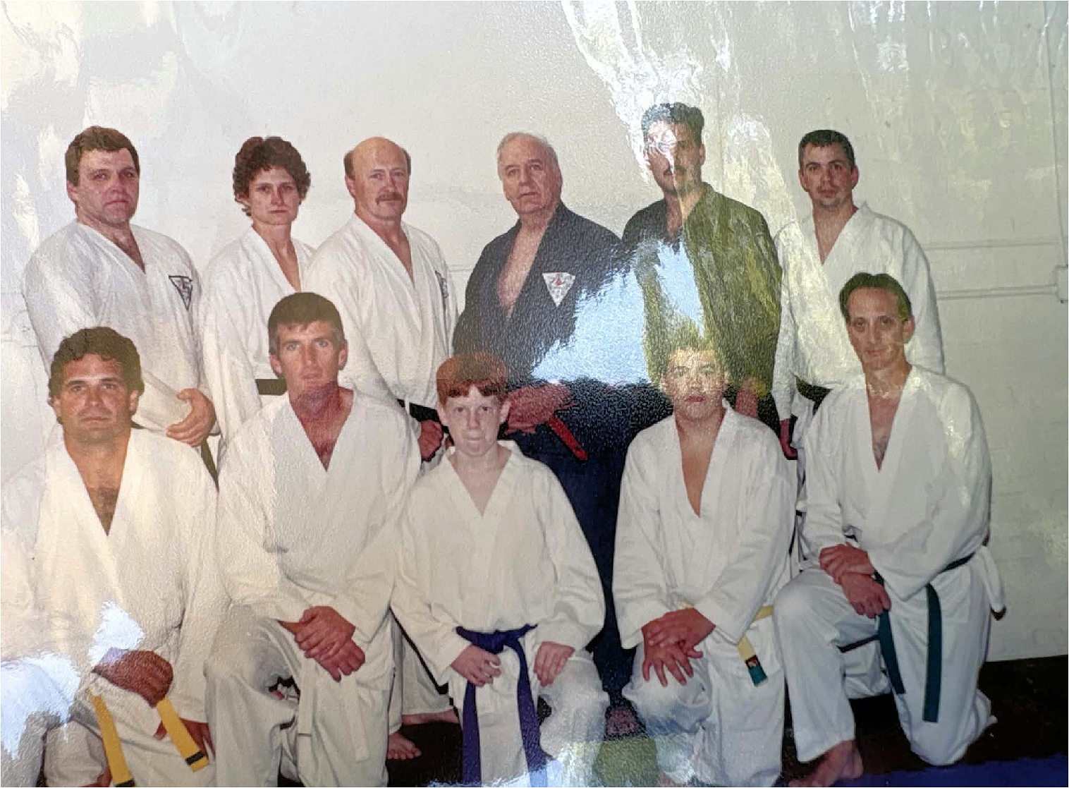 Group of martial artists in gi uniforms, some with belts, posing for a photo in a dojo or training space.