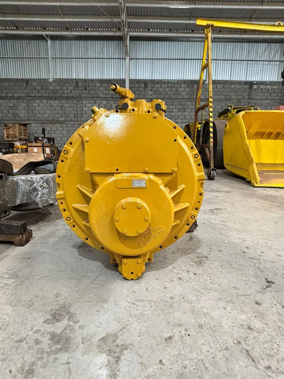 Tanque de color amarillo en un taller, con paredes de ladrillo y techo de metal, rodeado de otras piezas y herramientas.