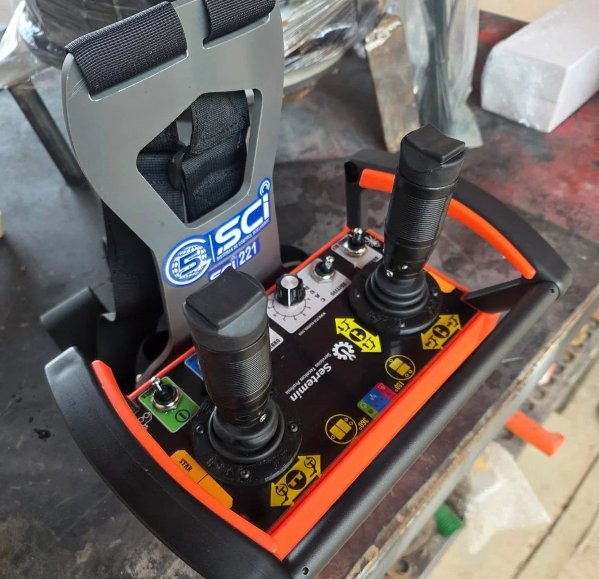 Control remoto con dos palancas, botones y etiquetas con instrucciones, sobre una mesa de trabajo.