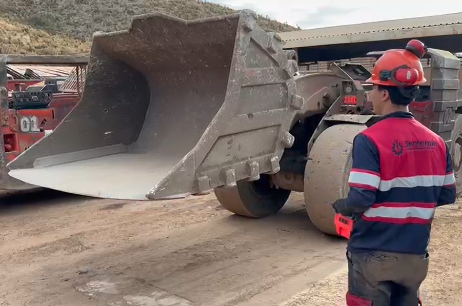 Persona con casco y equipo de seguridad observando una excavadora en un sitio de construcción.