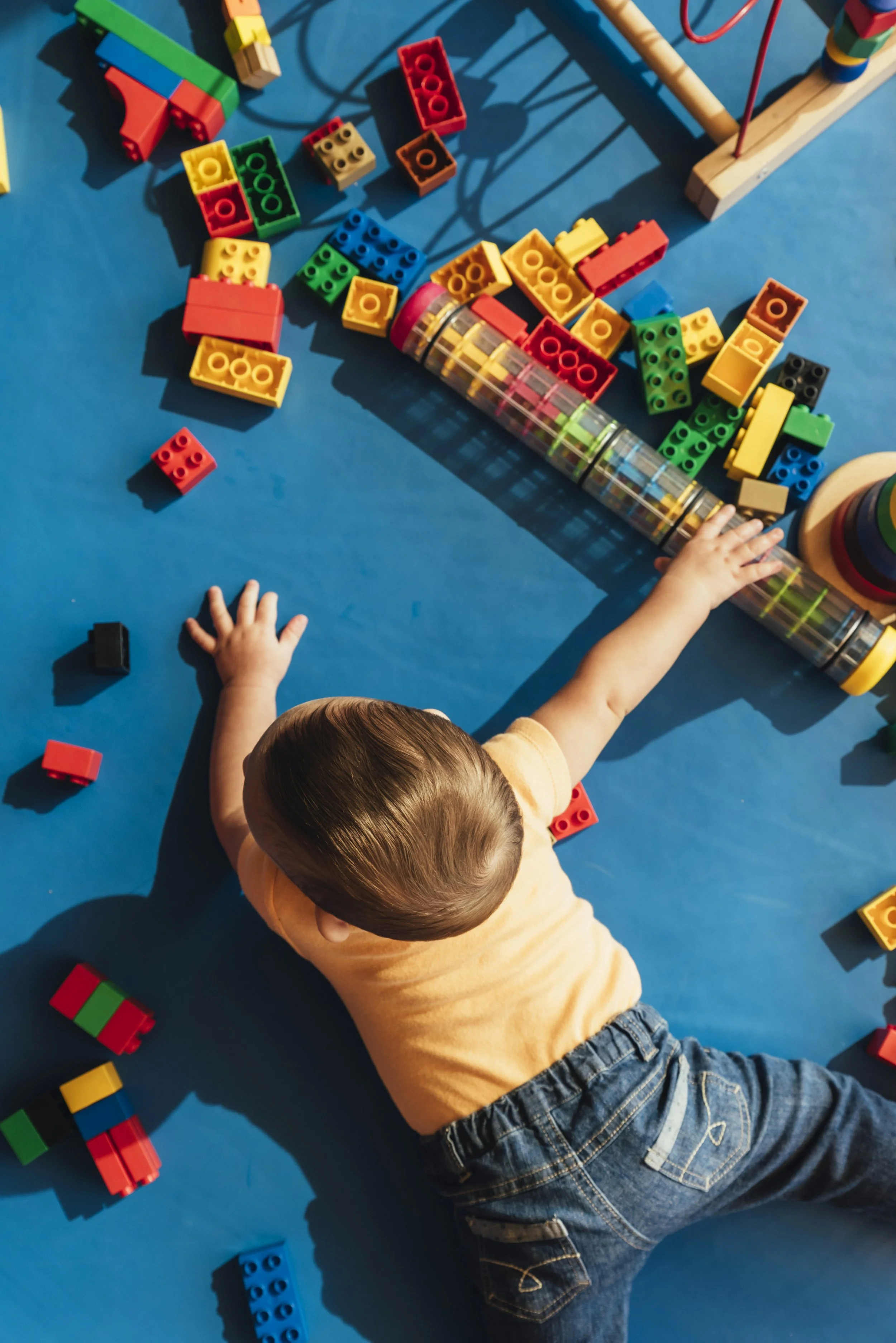 Child playing with colorful building blocks and a clear plastic tube on a blue floor.