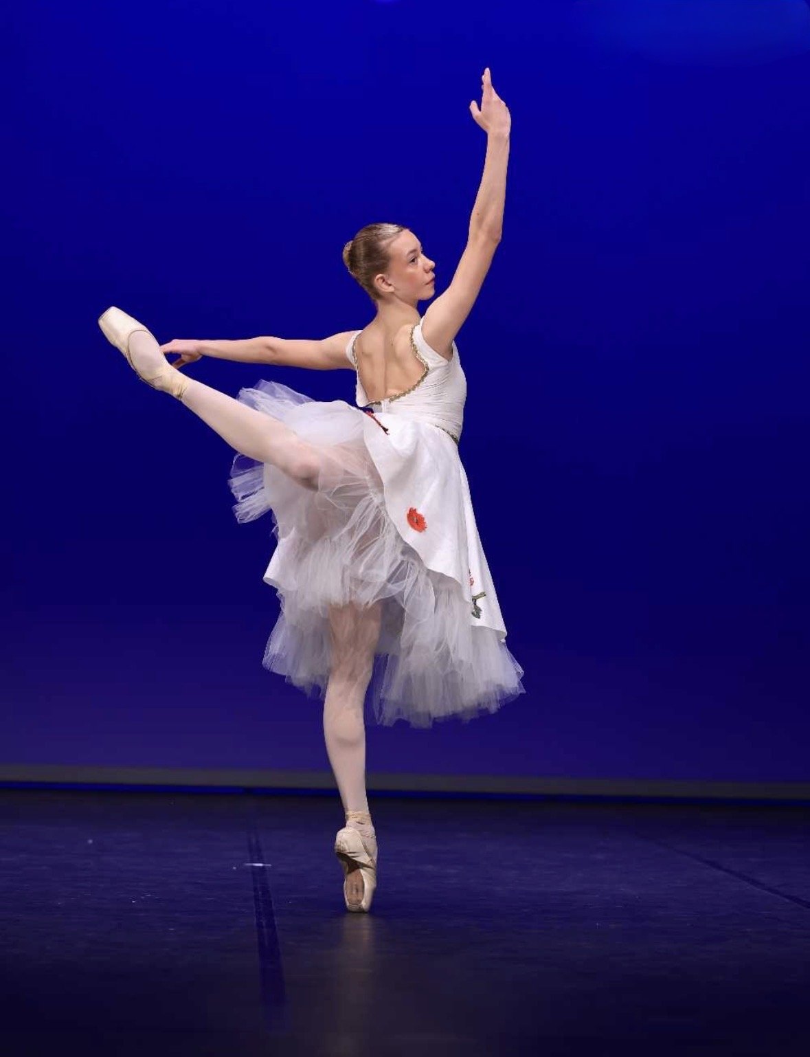 Balletdanser in witte tutu danst op een podium met een blauwe achtergrond.