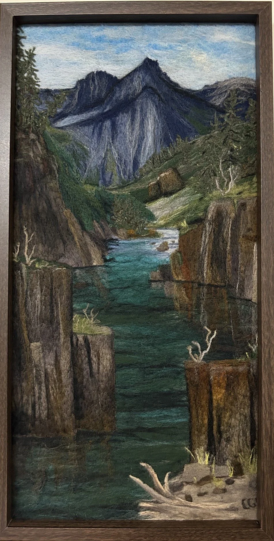 A landscape felting of a mountain scene with a river flowing through rocky basalt cliffs.