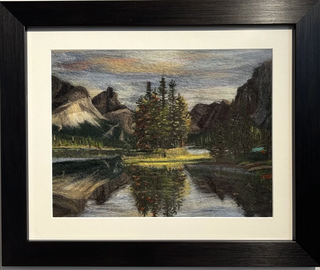 A needle felted landscape of Spirit Island reflecting autumn colours and Rocky Mountains, with a colorful sunset sky.