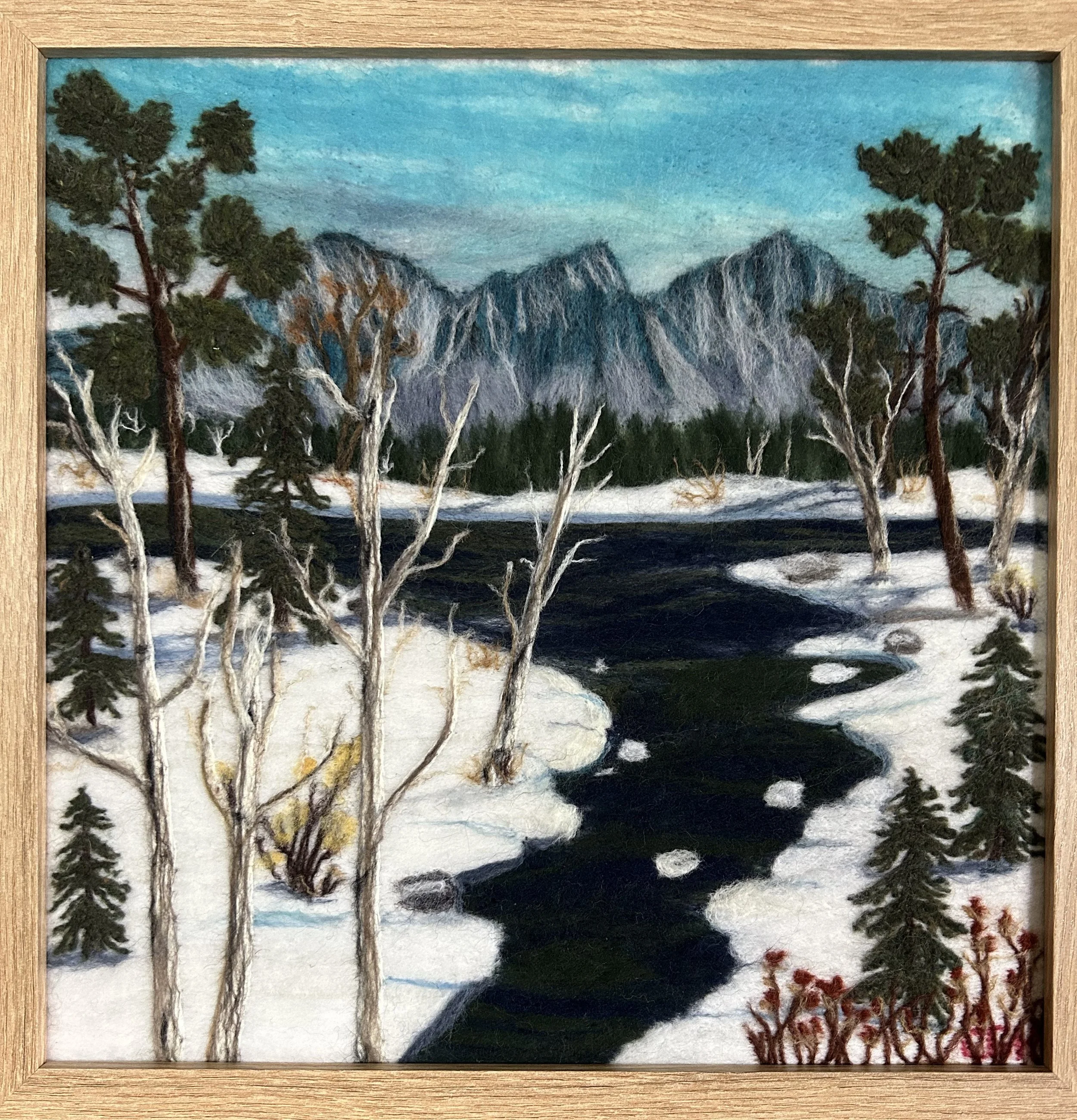 A wintery felted landscape of mountains, trees, and a river coming off the lake..
