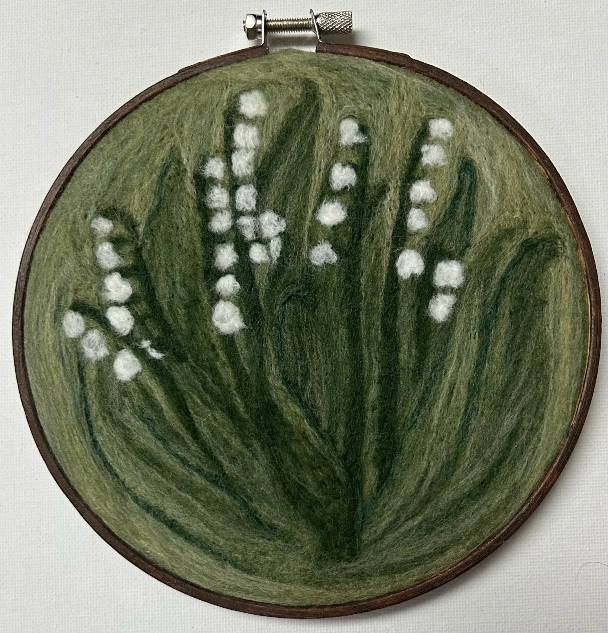 Small felted piece depicting Lily of the Valley flowers on a green background.
