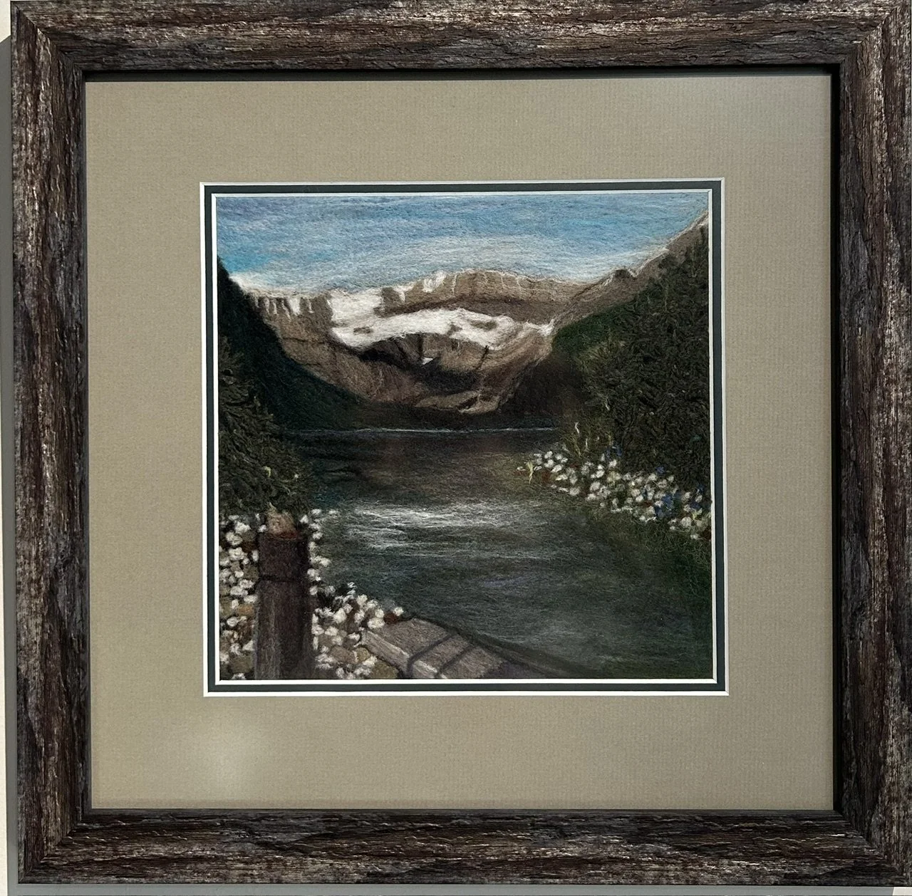Needle felted mountain landscape of Lake Louise with a clear blue sky and shaded lake, with a bench in the foreground