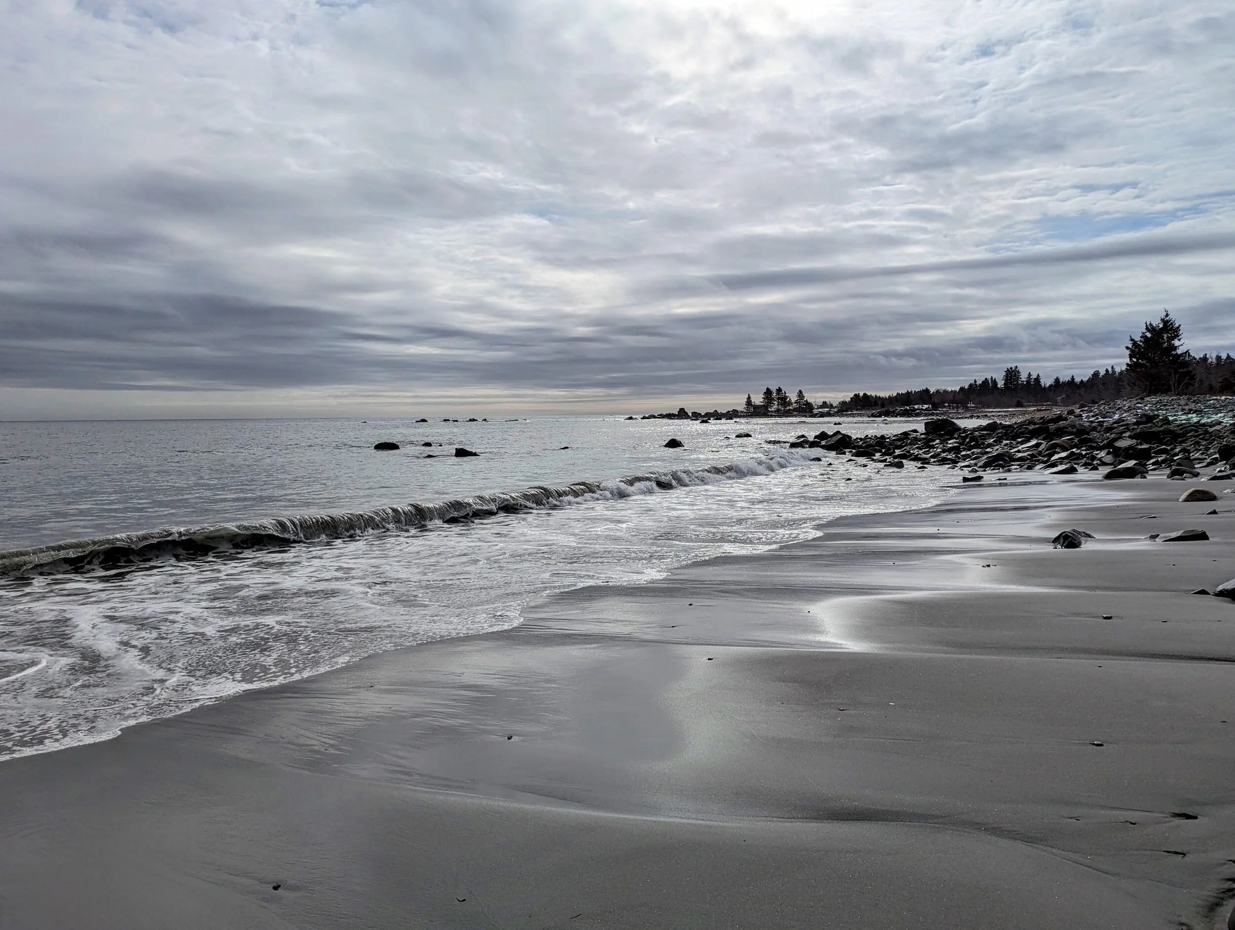 The Atlantic on a grey February day, waves washing over wet sand and snow along the shore.