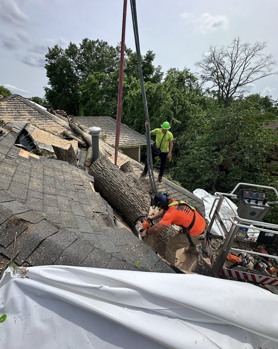 Tree falling on roof of house during storm, with rescue workers cutting the tree and inspecting the damage.