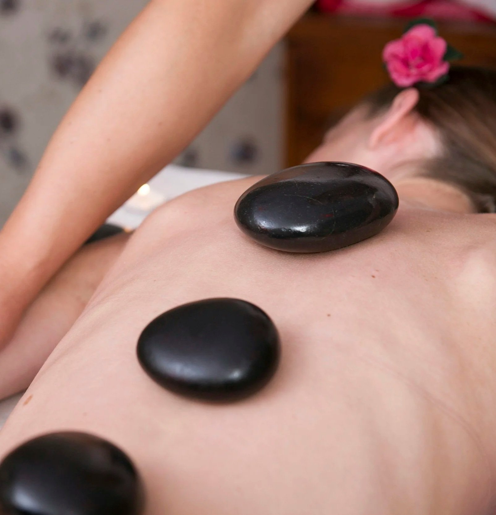 Close-up of a person's back with black hot stones placed along the spine during a massage.