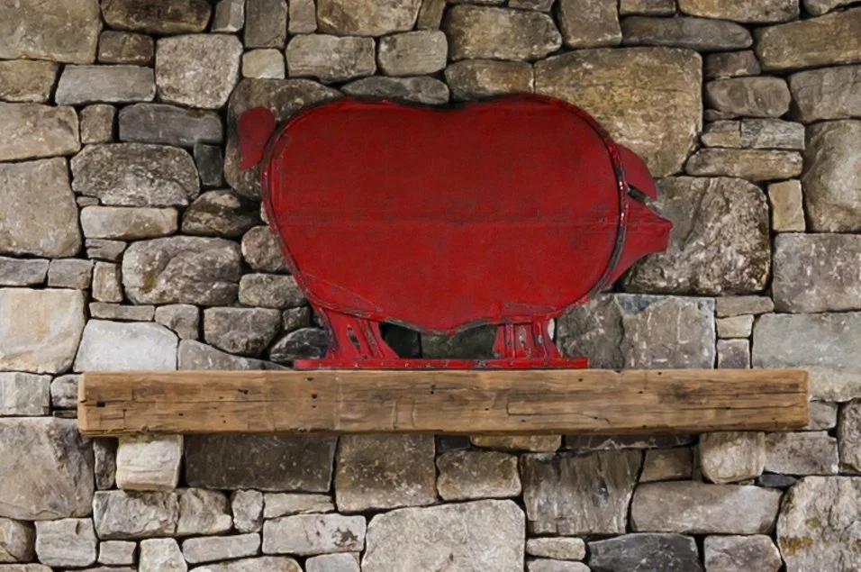 A red piggy bank shaped like a pig on a wooden shelf against a stone wall.