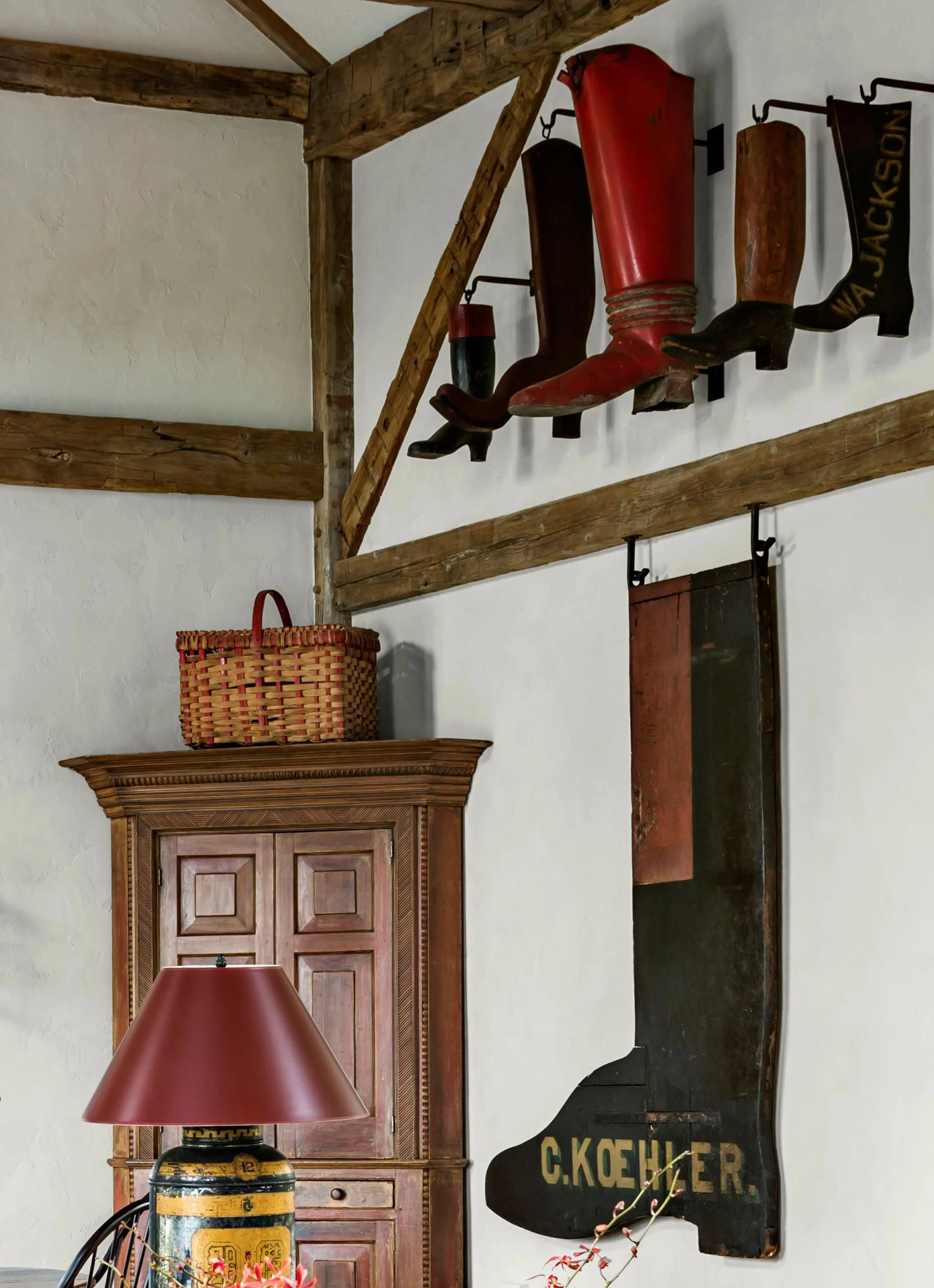 Interior of a converted barn with a large collection of antique shoemakers' trade signs, all in the form of boots, mounted on iron hooks.  The corner of the room features an 18th century corner cupboard with original red paint, and antique basket.