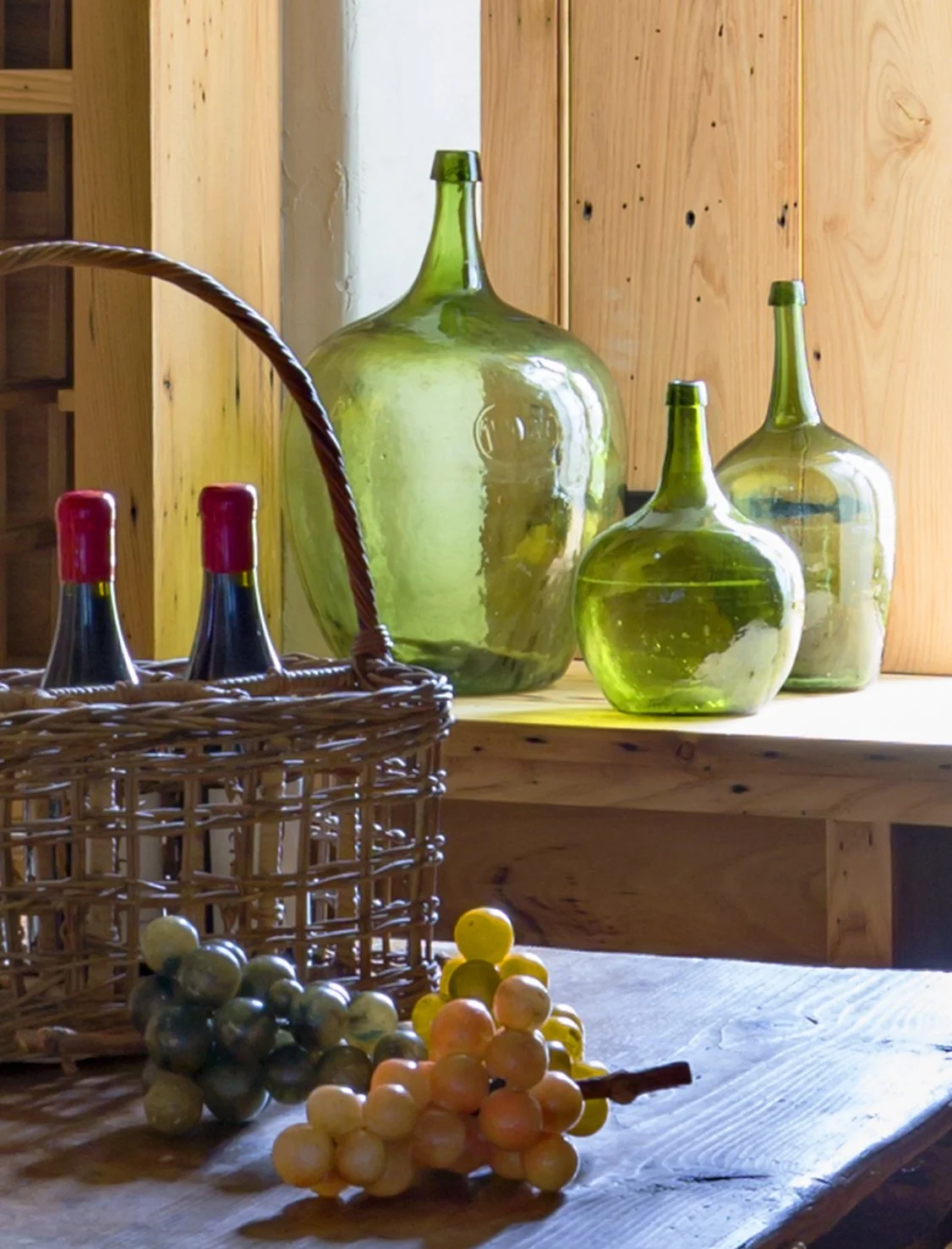 A display of 19th century hand-blown bottles and hand-carved alabaster grapes in a wine cellar with chestnut walls.