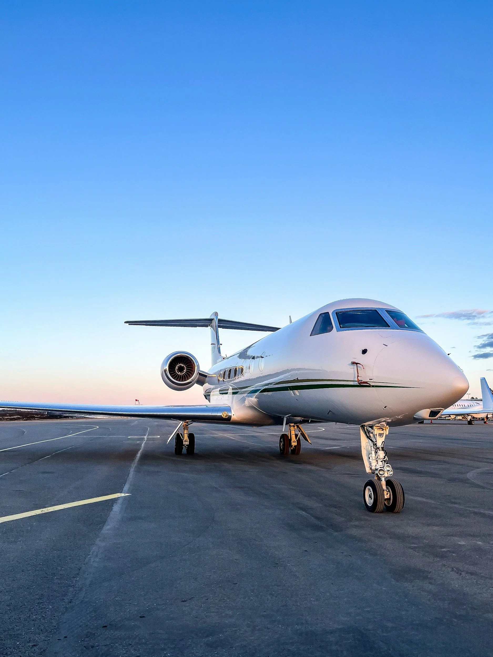 A white private jet parked on an airport tarmac during sunset with a clear blue sky.