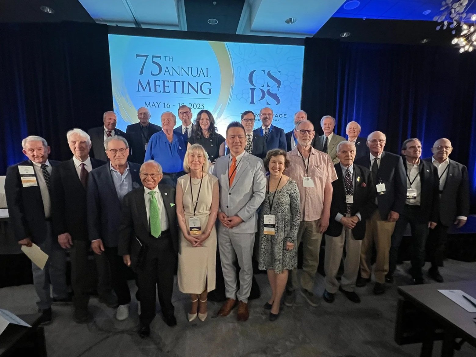 Group of past presidents attending the 75th annual meeting, May 16-18, 2025, posing on a stage with a large screen behind them displaying event details and logo