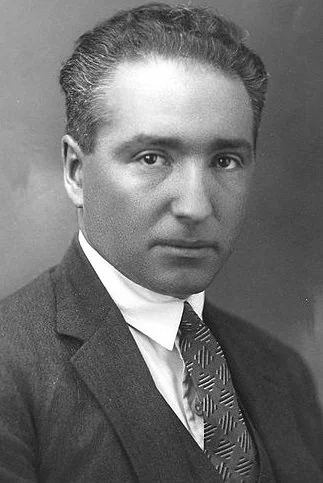 Black and white portrait of a man in a suit and tie, with neatly styled hair and a serious expression.