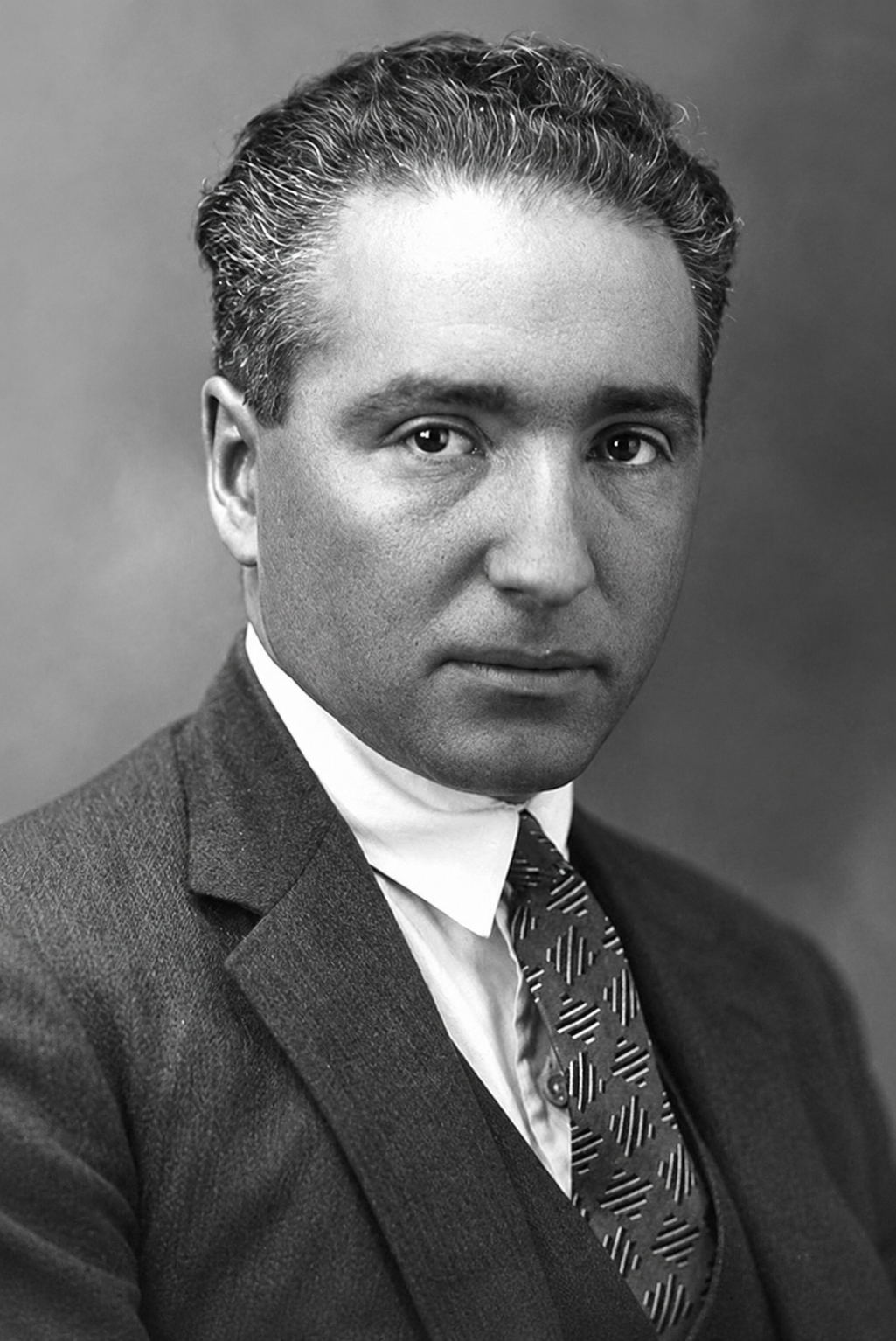 Black and white portrait of a man in a suit and tie looking directly at the camera.