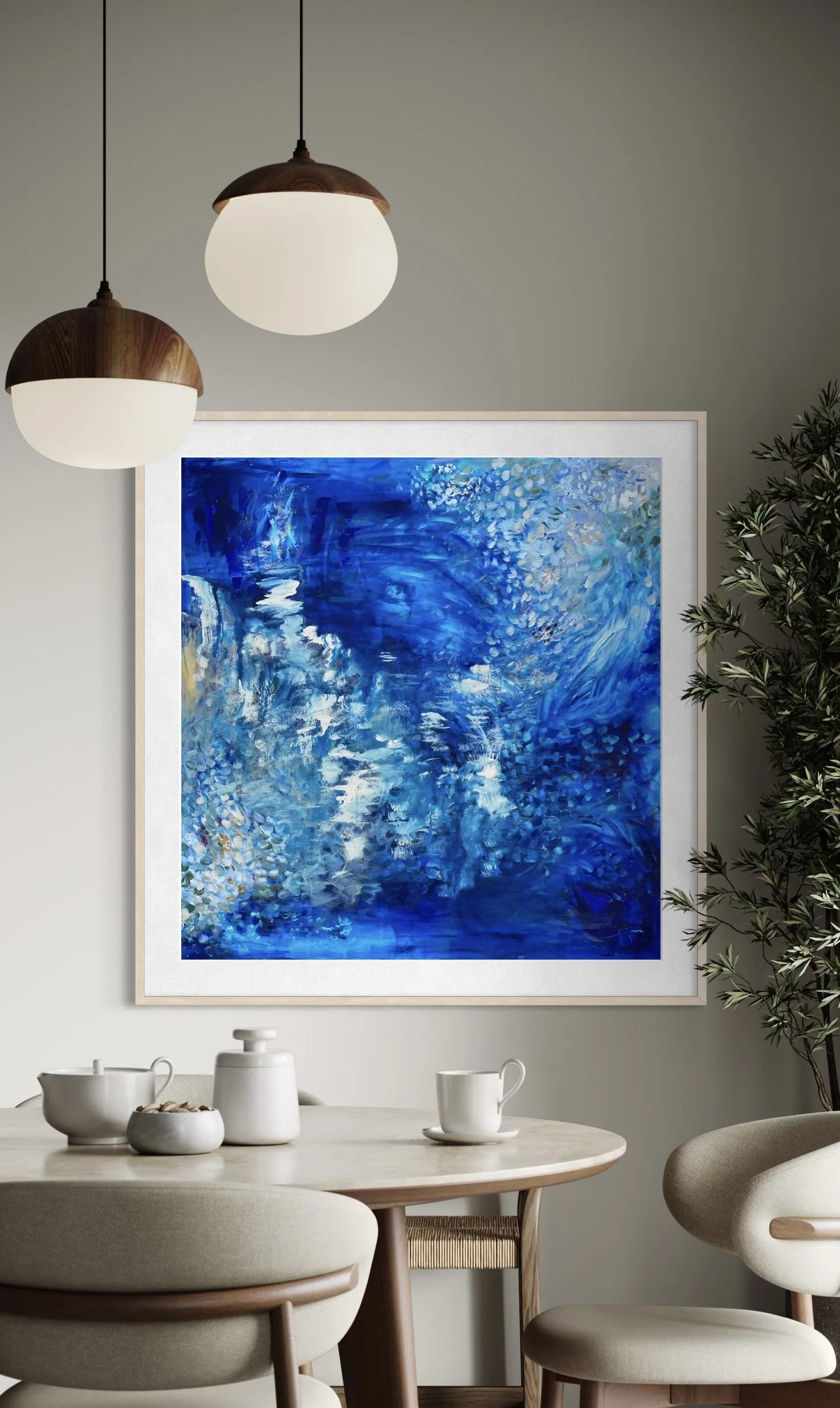 Pintura abstracta en tonos azules en una pared, junto a una mesa redonda con tazas y jarrones blancos, y una planta grande a la derecha, en un comedor moderno.