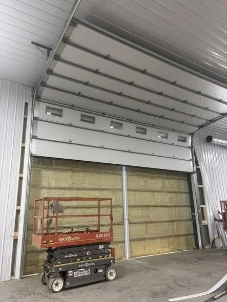 An open industrial garage door with a scissor lift parked inside in a warehouse.