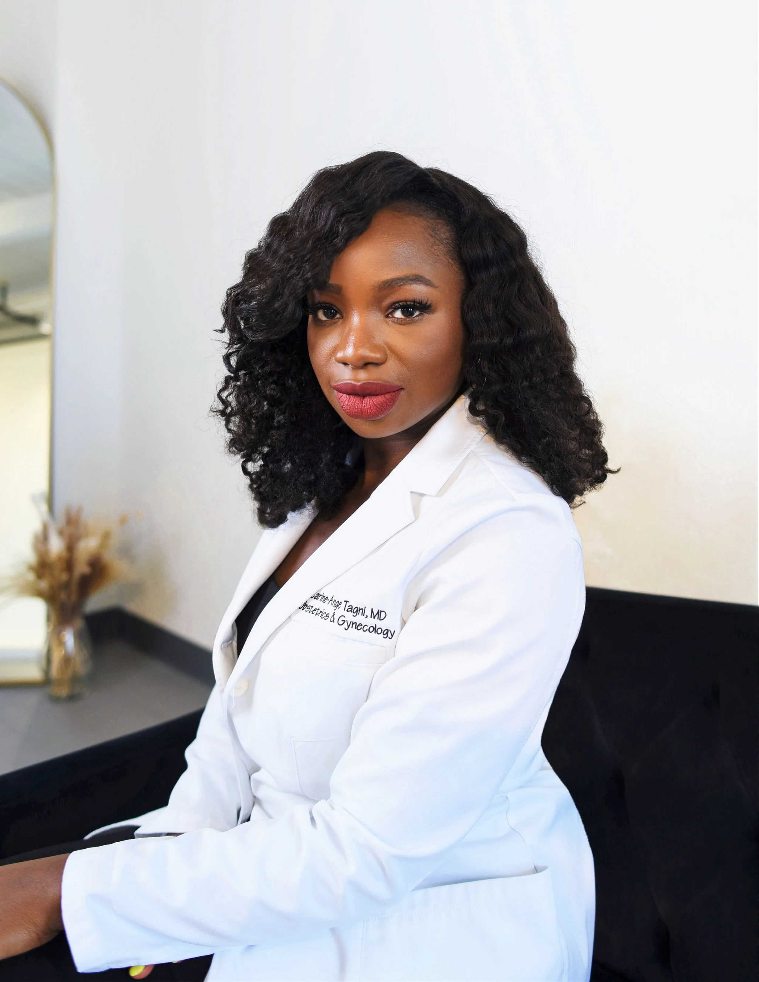 Dr. Carine-Ange Tagni, board certified OBGYN, seated in her white coat