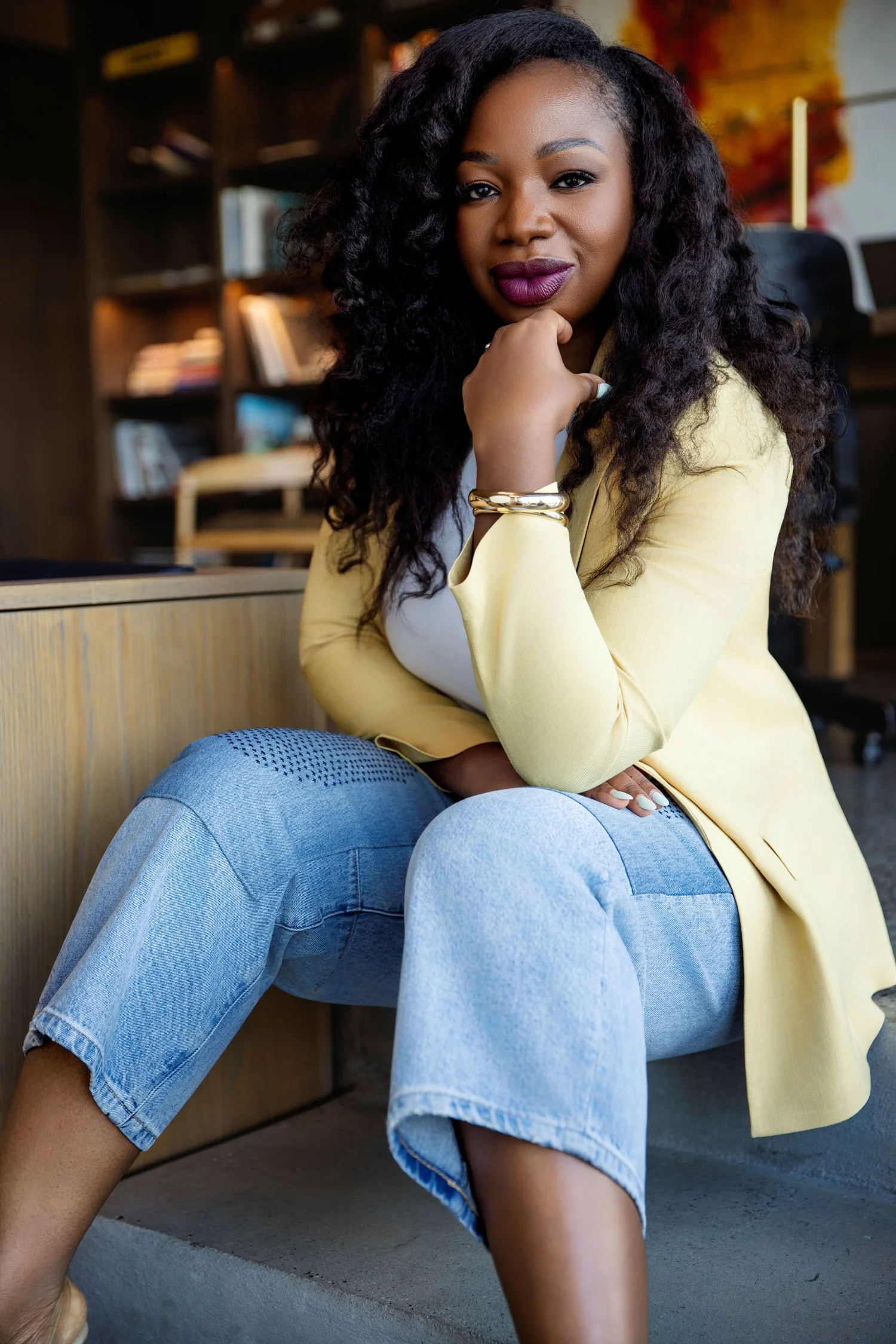 Dr. Carine-Ange Tagni seated in a yellow blazer, chin resting on her hand